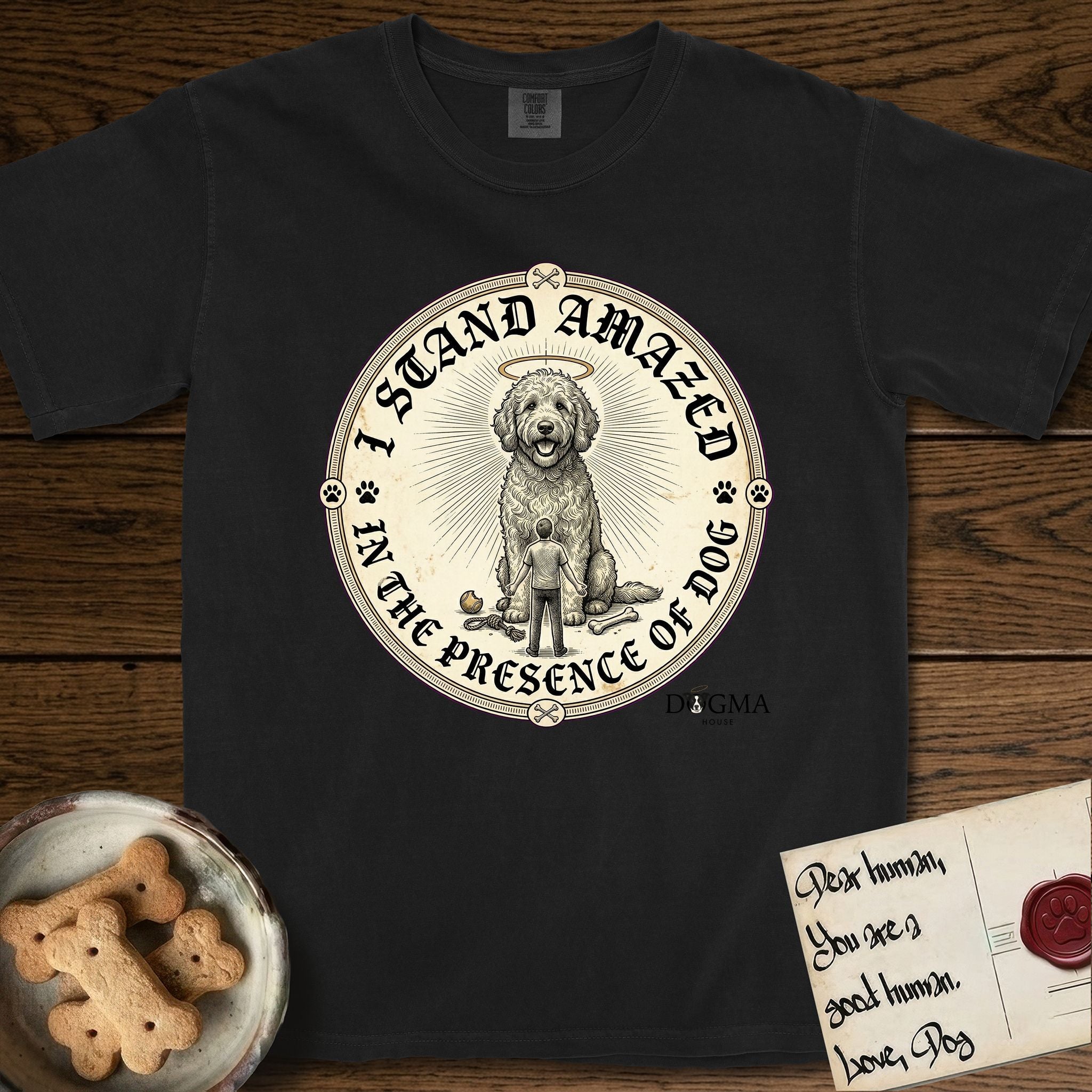 I Stand Amazed in the Presence Goldendoodle T-Shirt flat lay in Black, featuring a vintage engraving medallion of a haloed Goldendoodle with a small devoted human gazing up from below.