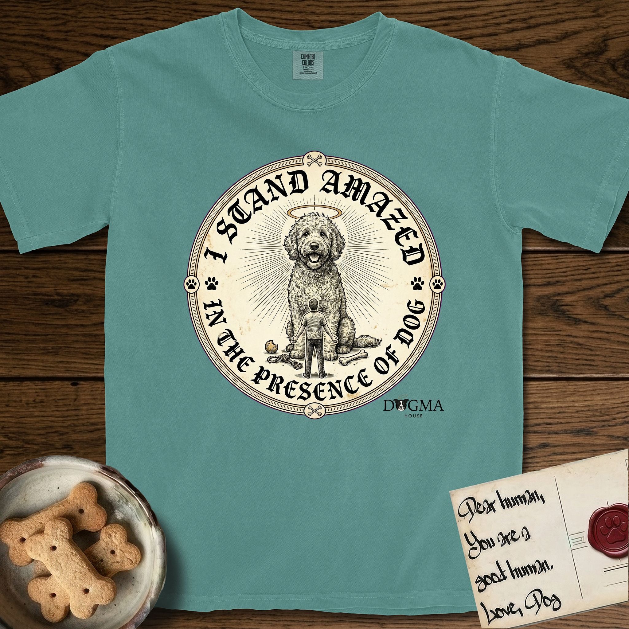 I Stand Amazed in the Presence Goldendoodle T-Shirt flat lay in Blue Spruce, featuring a vintage engraving medallion of a haloed Goldendoodle with a small devoted human gazing up from below.