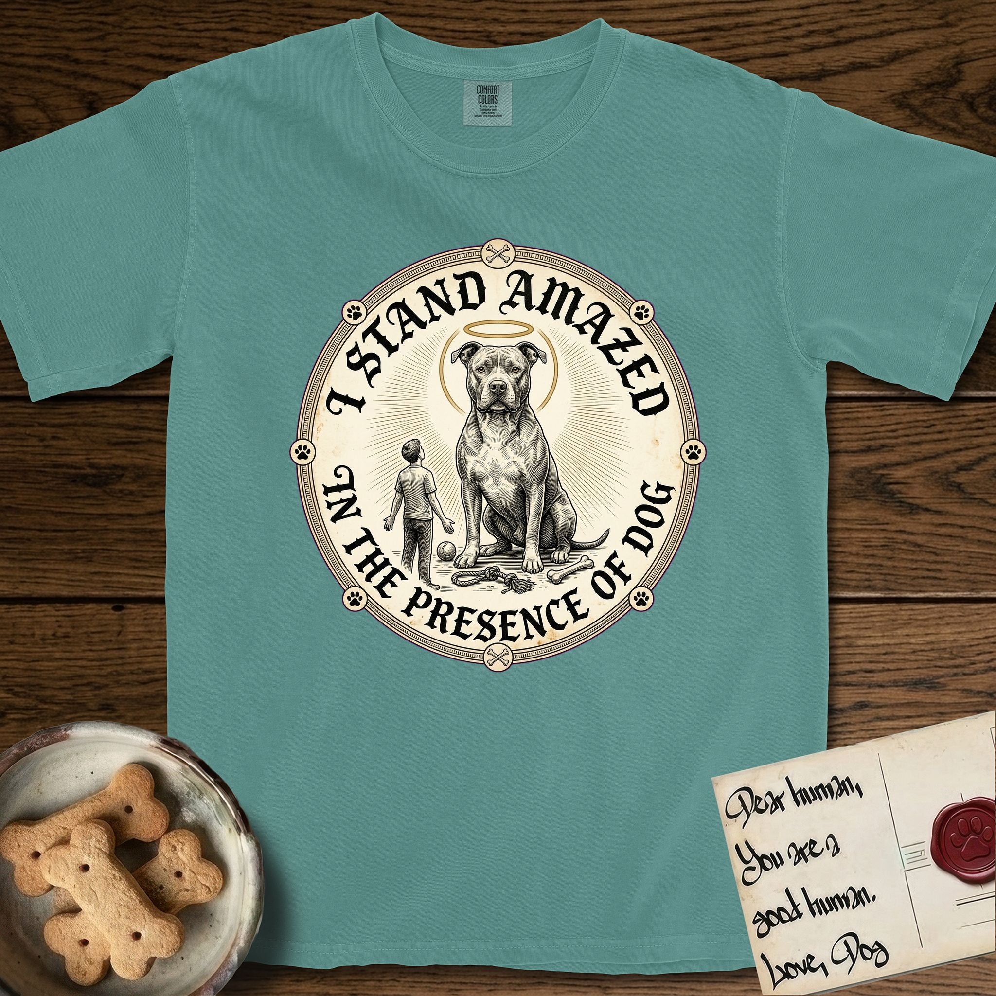 I Stand Amazed in the Presence Pitbull T-Shirt flat lay in Blue Spruce, featuring a vintage engraving medallion of a haloed Pitbull with a small devoted human gazing up from below.
