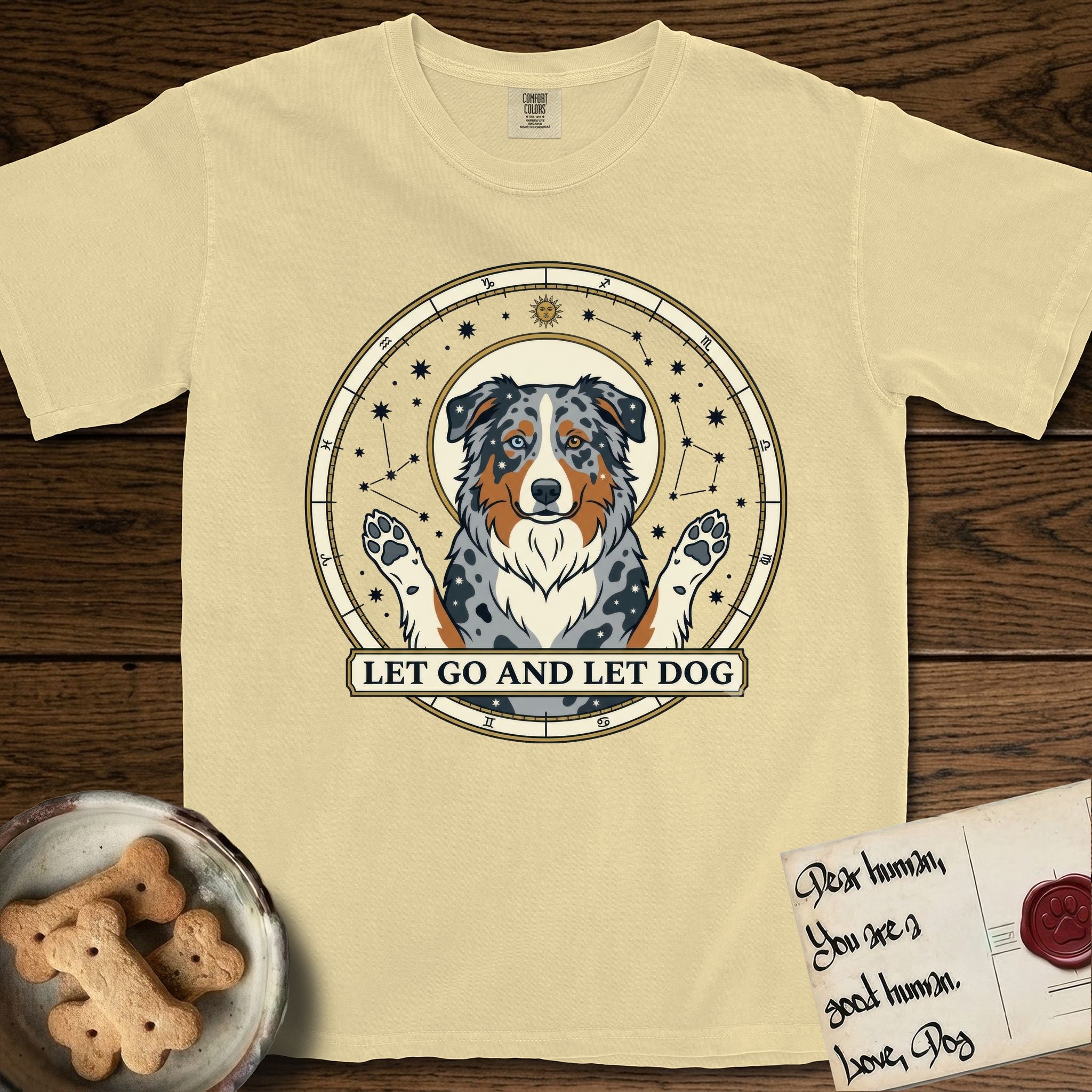 Let Go and Let Dog Australian Shepherd T-Shirt flat lay in Butter, featuring an antique celestial star chart with a haloed blue merle Australian Shepherd at the center, paws raised, stars scattered through her coat.