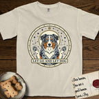 Let Go and Let Dog Australian Shepherd T-Shirt flat lay in Ivory, featuring an antique celestial star chart with a haloed blue merle Australian Shepherd at the center, paws raised, stars scattered through her coat.