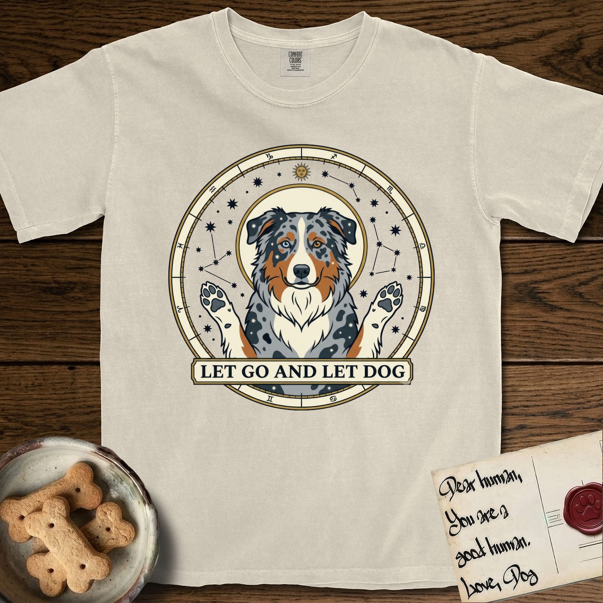 Let Go and Let Dog Australian Shepherd T-Shirt flat lay in Ivory, featuring an antique celestial star chart with a haloed blue merle Australian Shepherd at the center, paws raised, stars scattered through her coat.