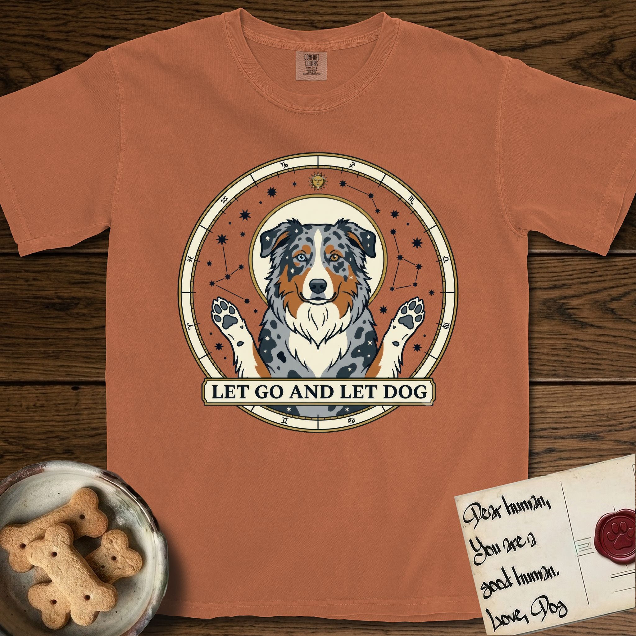 Let Go and Let Dog Australian Shepherd T-Shirt flat lay in Yam, featuring an antique celestial star chart with a haloed blue merle Australian Shepherd at the center, paws raised, stars scattered through her coat.