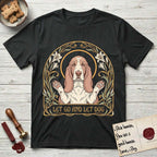 Let Go and Let Dog Basset Hound T-Shirt flat lay in Black, featuring an Art Nouveau botanical illustration of a haloed Basset Hound with paws raised in blessing.