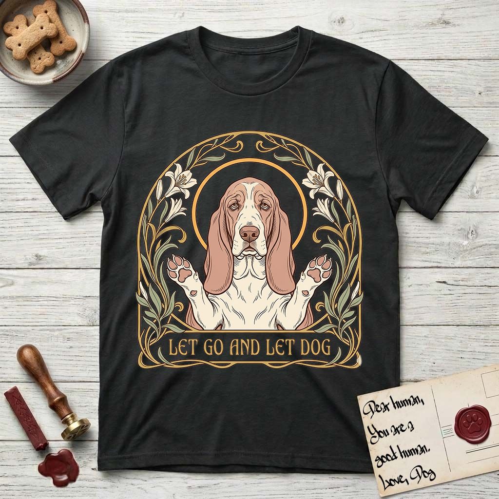Let Go and Let Dog Basset Hound T-Shirt flat lay in Black, featuring an Art Nouveau botanical illustration of a haloed Basset Hound with paws raised in blessing.
