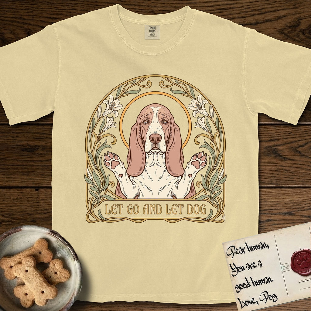 Let Go and Let Dog Basset Hound T-Shirt flat lay in Butter, featuring an Art Nouveau botanical illustration of a haloed Basset Hound with paws raised in blessing.