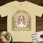 Let Go and Let Dog Basset Hound T-Shirt flat lay in Butter, featuring an Art Nouveau botanical illustration of a haloed Basset Hound with paws raised in blessing.