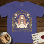 Let Go and Let Dog Basset Hound T-Shirt flat lay in Grape, featuring an Art Nouveau botanical illustration of a haloed Basset Hound with paws raised in blessing.