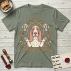 Let Go and Let Dog Basset Hound T-Shirt flat lay in Sage, featuring an Art Nouveau botanical illustration of a haloed Basset Hound with paws raised in blessing.