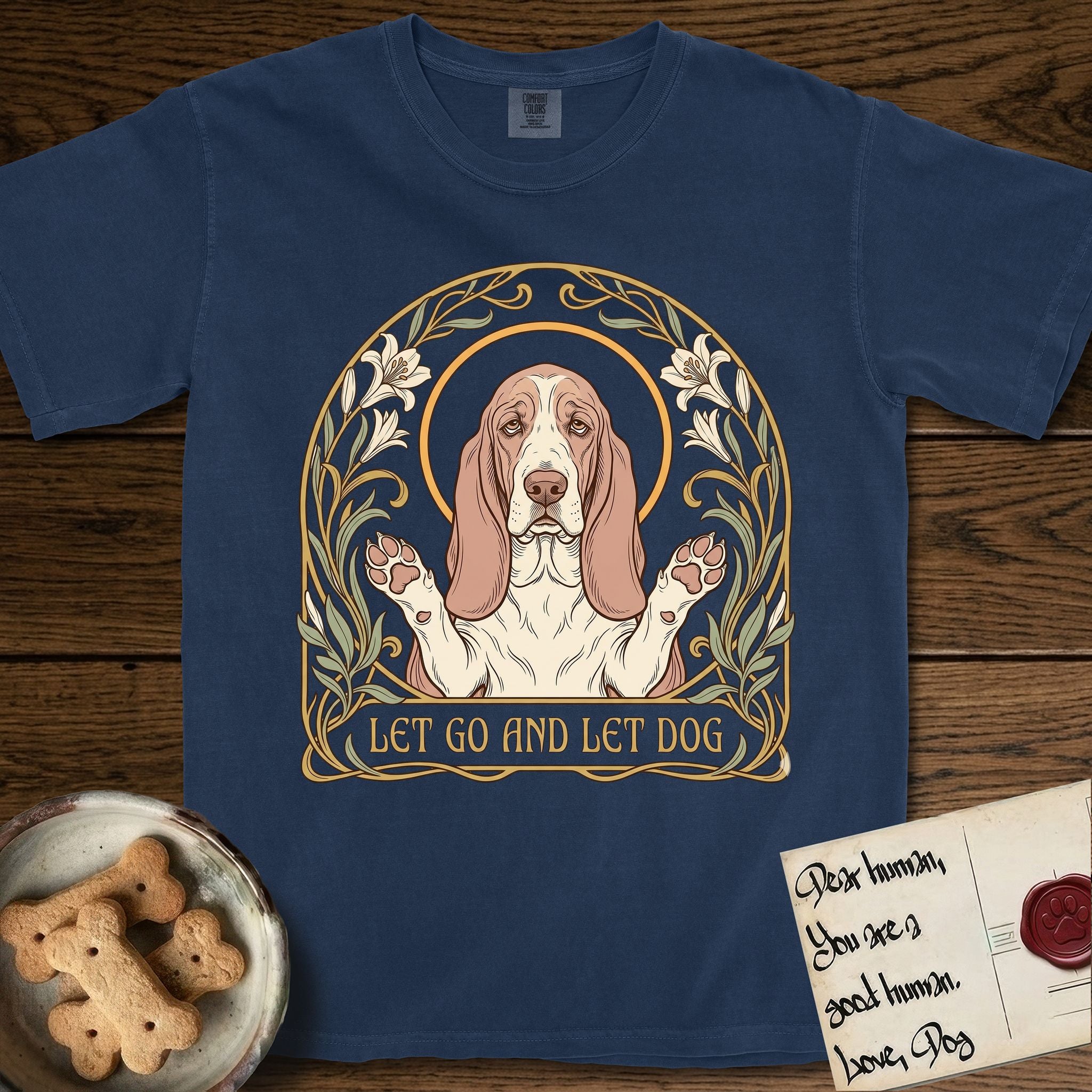 Let Go and Let Dog Basset Hound T-Shirt flat lay in True Navy, featuring an Art Nouveau botanical illustration of a haloed Basset Hound with paws raised in blessing.