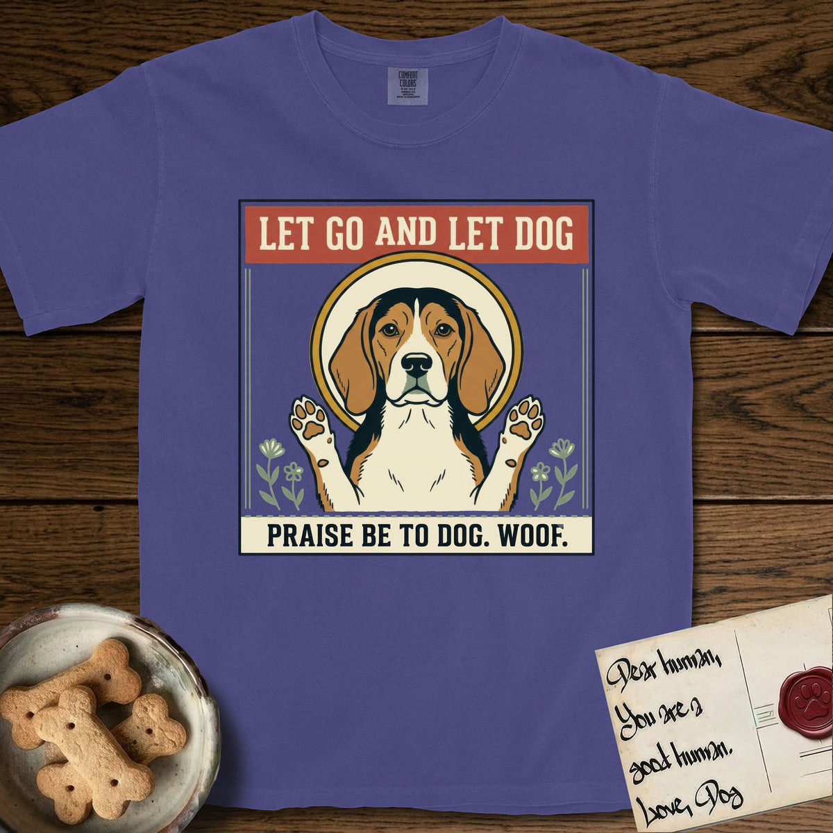 Let Go and Let Dog Beagle T-Shirt flat lay in Grape, featuring a vintage seed packet label with a haloed tricolor Beagle, paws raised, flanked by simple flower sprigs.