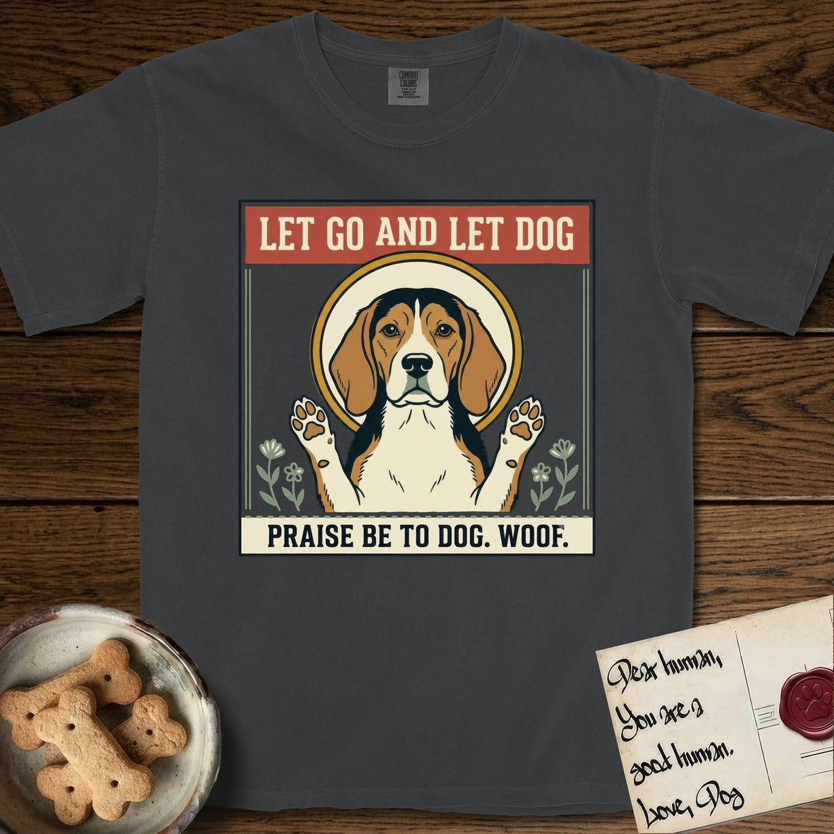 Let Go and Let Dog Beagle T-Shirt flat lay in Graphite, featuring a vintage seed packet label with a haloed tricolor Beagle, paws raised, flanked by simple flower sprigs.