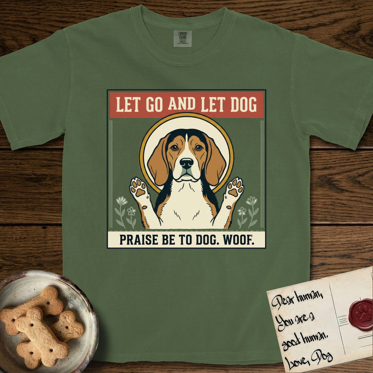 Let Go and Let Dog Beagle T-Shirt flat lay in Moss, featuring a vintage seed packet label with a haloed tricolor Beagle, paws raised, flanked by simple flower sprigs.