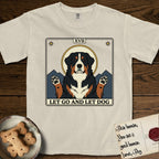 Let Go and Let Dog Bernese Mountain Dog T-Shirt flat lay in Ivory, featuring a vintage tarot card with a haloed tricolor Bernese Mountain Dog, paws raised, mountains rising behind her shoulders.