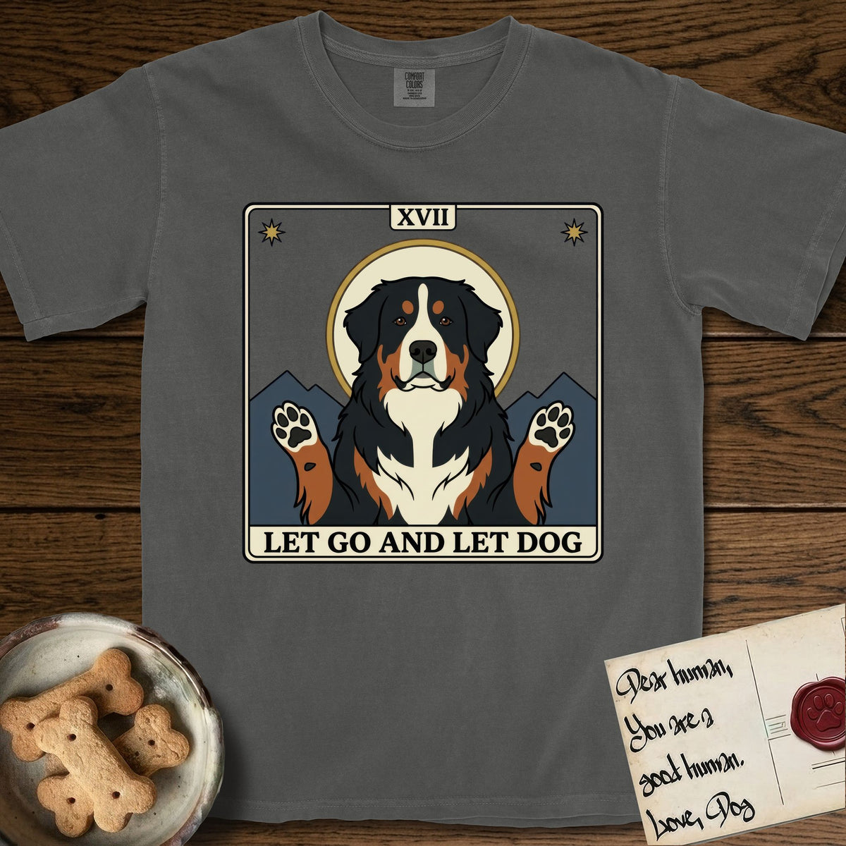 Let Go and Let Dog Bernese Mountain Dog T-Shirt flat lay in Pepper, featuring a vintage tarot card with a haloed tricolor Bernese Mountain Dog, paws raised, mountains rising behind her shoulders.