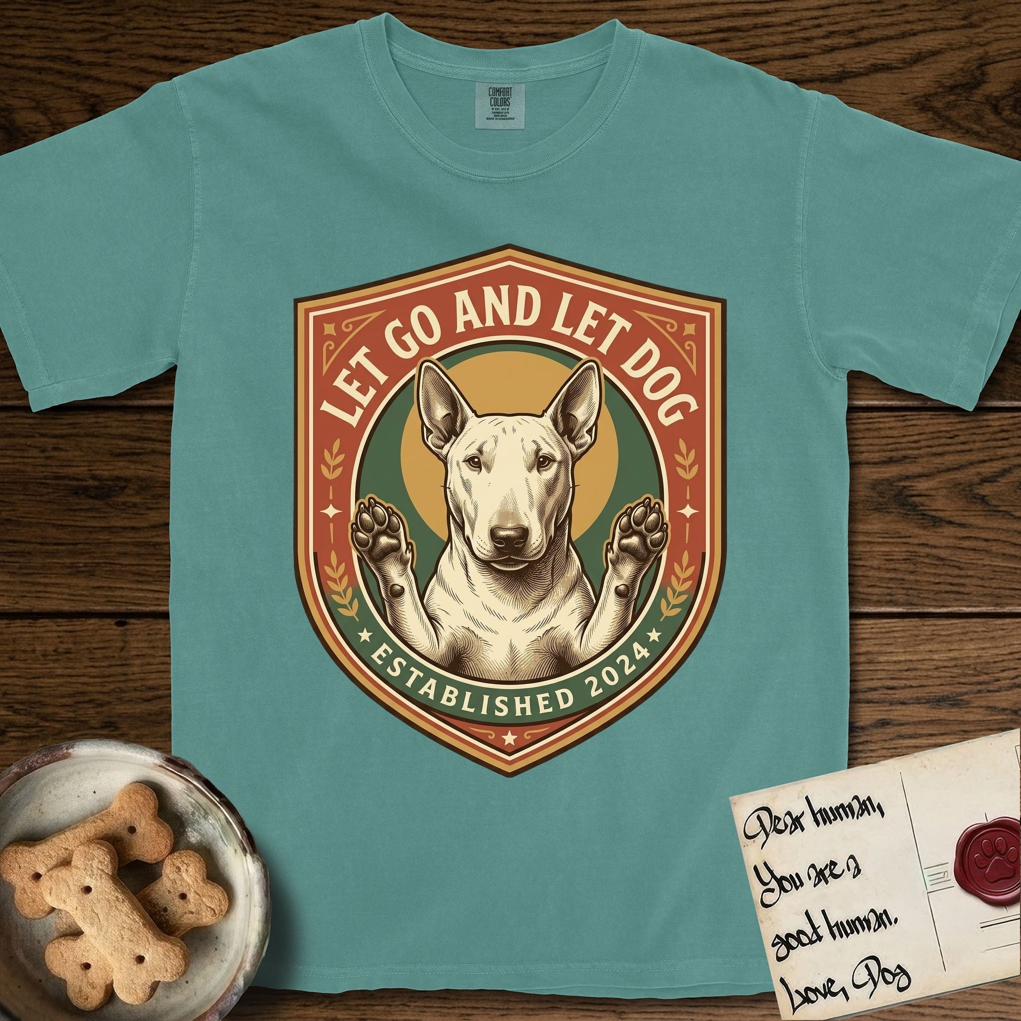 Let Go and Let Dog Bull Terrier T-Shirt flat lay in Blue Spruce, featuring a vintage badge of a haloed Bull Terrier with paws raised in blessing.