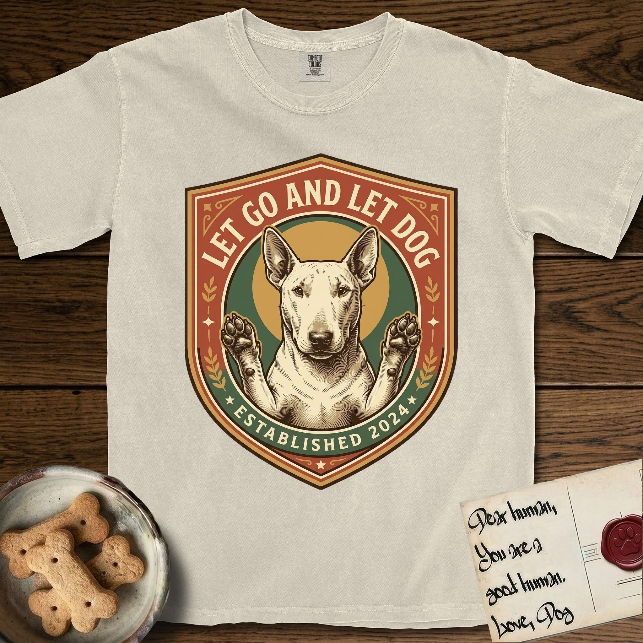 Let Go and Let Dog Bull Terrier T-Shirt flat lay in Ivory, featuring a vintage badge of a haloed Bull Terrier with paws raised in blessing.