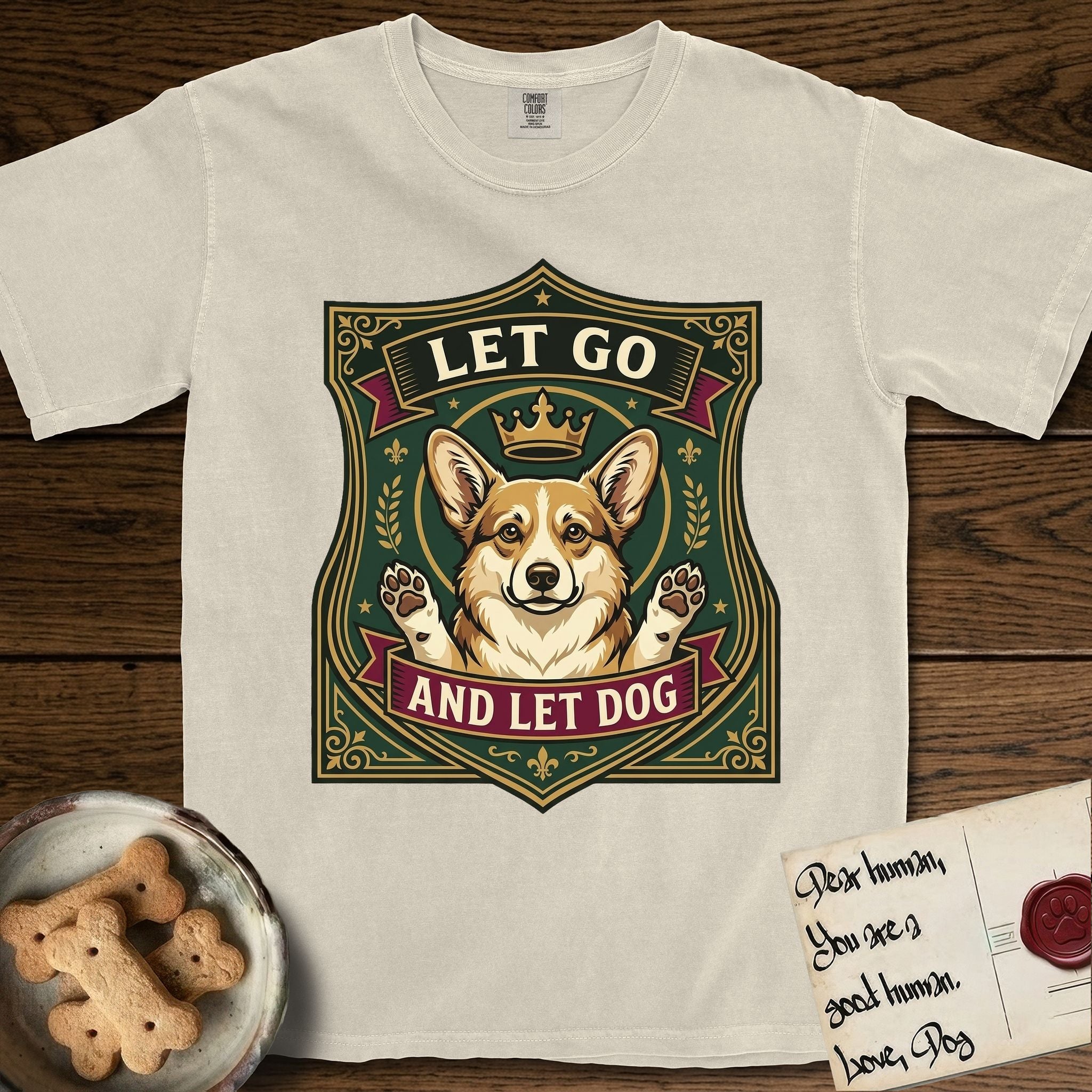 Let Go and Let Dog Corgi T-Shirt flat lay in Ivory, featuring a royal heraldic shield badge of a crowned, haloed Corgi with paws raised.