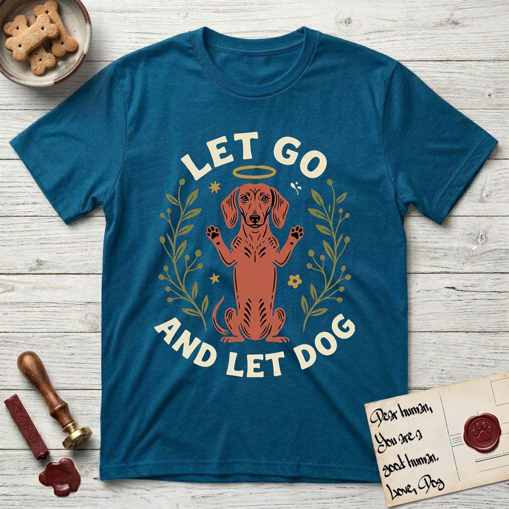 Let Go and Let Dog Dachshund T-Shirt flat lay in Antique Sapphire, featuring a folk-art botanical illustration of a haloed Dachshund sitting up with front paws raised.