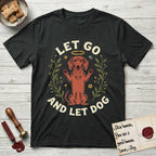 Let Go and Let Dog Dachshund T-Shirt flat lay in Black, featuring a folk-art botanical illustration of a haloed Dachshund sitting up with front paws raised.