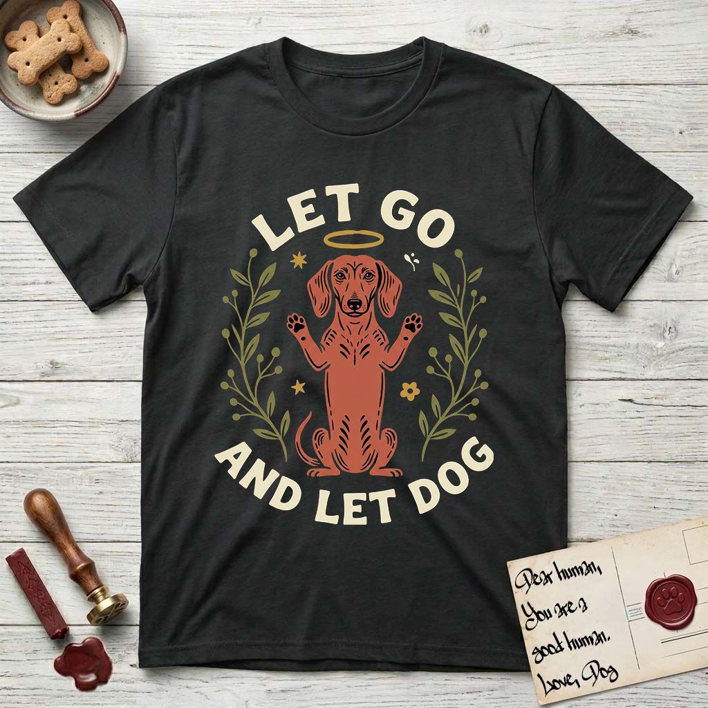 Let Go and Let Dog Dachshund T-Shirt flat lay in Black, featuring a folk-art botanical illustration of a haloed Dachshund sitting up with front paws raised.