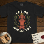 Let Go and Let Dog Dachshund T-Shirt flat lay in Black, featuring a folk-art botanical illustration of a haloed Dachshund sitting up with front paws raised.