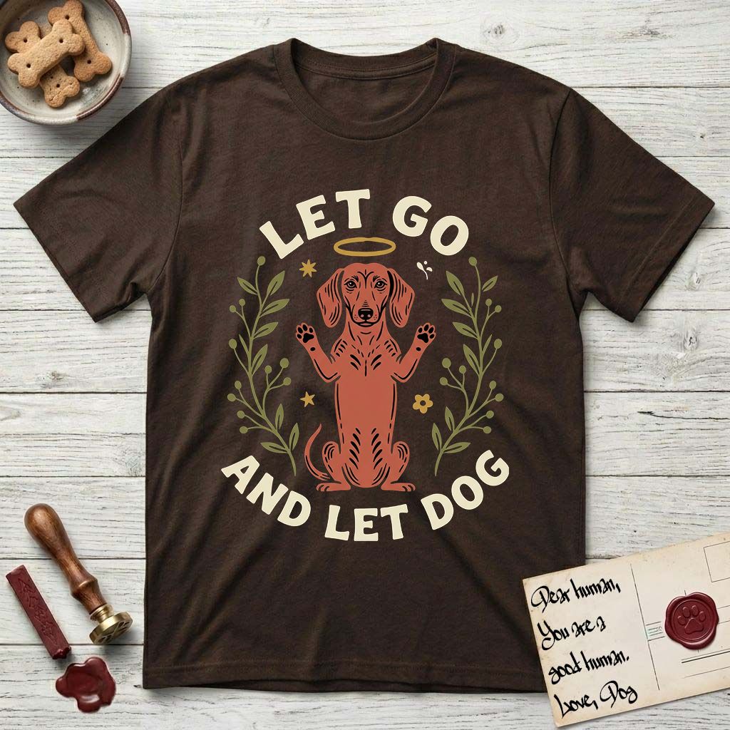 Let Go and Let Dog Dachshund T-Shirt flat lay in Dark Chocolate, featuring a folk-art botanical illustration of a haloed Dachshund sitting up with front paws raised.