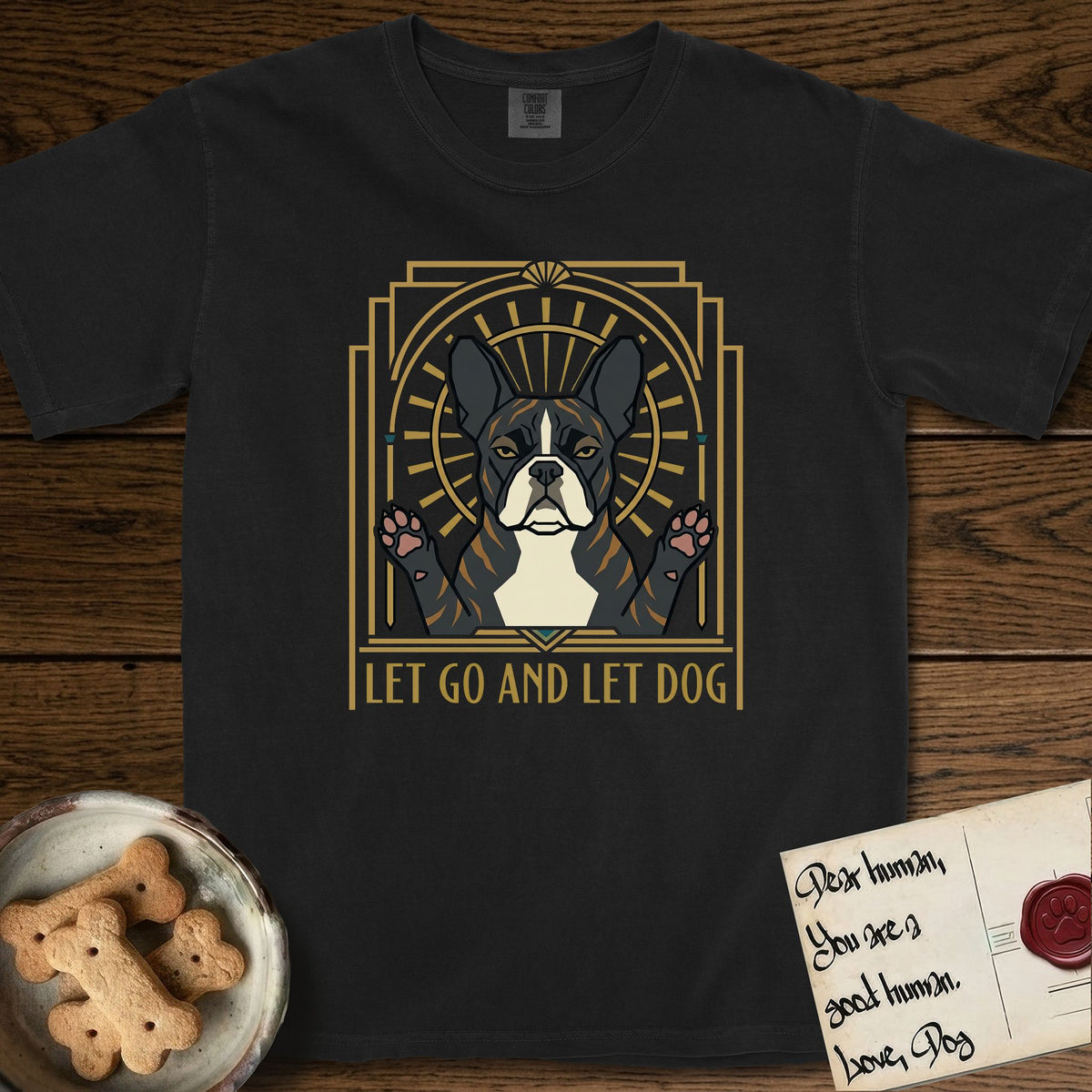 Let Go and Let Dog French Bulldog T-Shirt flat lay in Black, featuring an Art Deco arch with a haloed brindle French Bulldog, bat ears erect and paws raised, gold sunburst rays behind him.