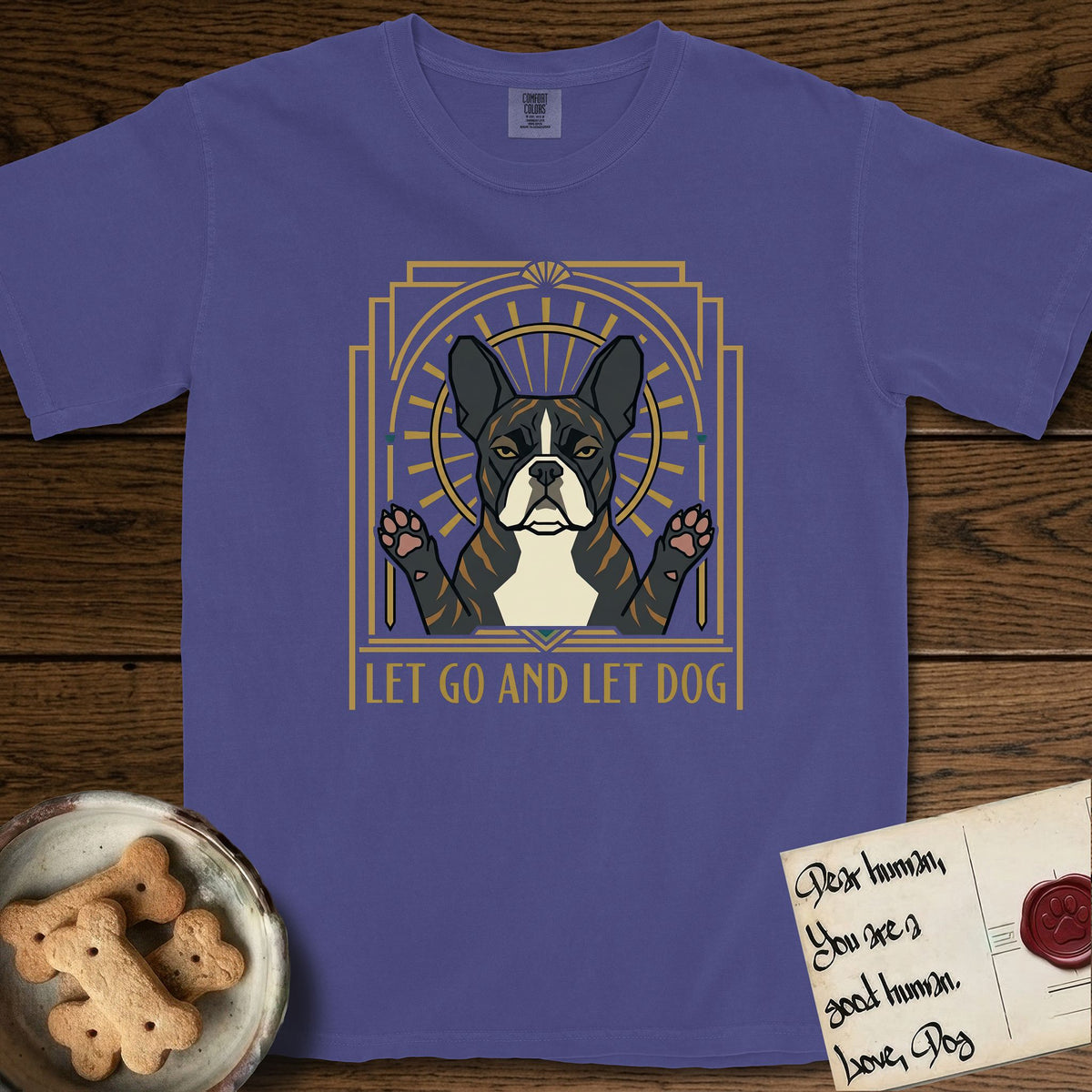 Let Go and Let Dog French Bulldog T-Shirt flat lay in Grape, featuring an Art Deco arch with a haloed brindle French Bulldog, bat ears erect and paws raised, gold sunburst rays behind him.