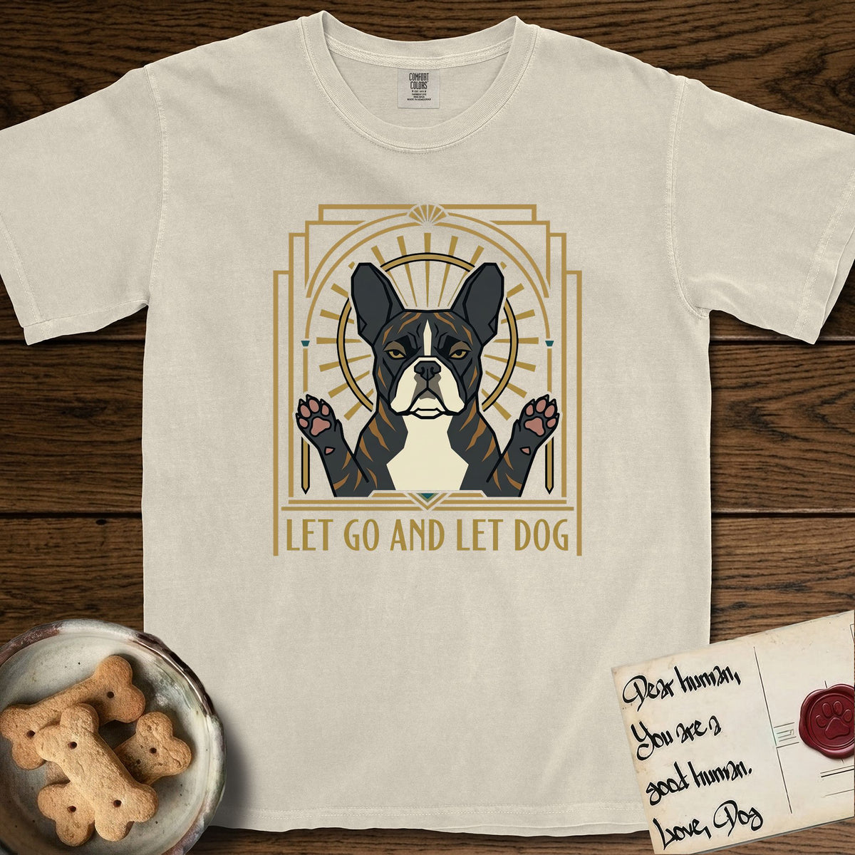Let Go and Let Dog French Bulldog T-Shirt flat lay in Ivory, featuring an Art Deco arch with a haloed brindle French Bulldog, bat ears erect and paws raised, gold sunburst rays behind him.