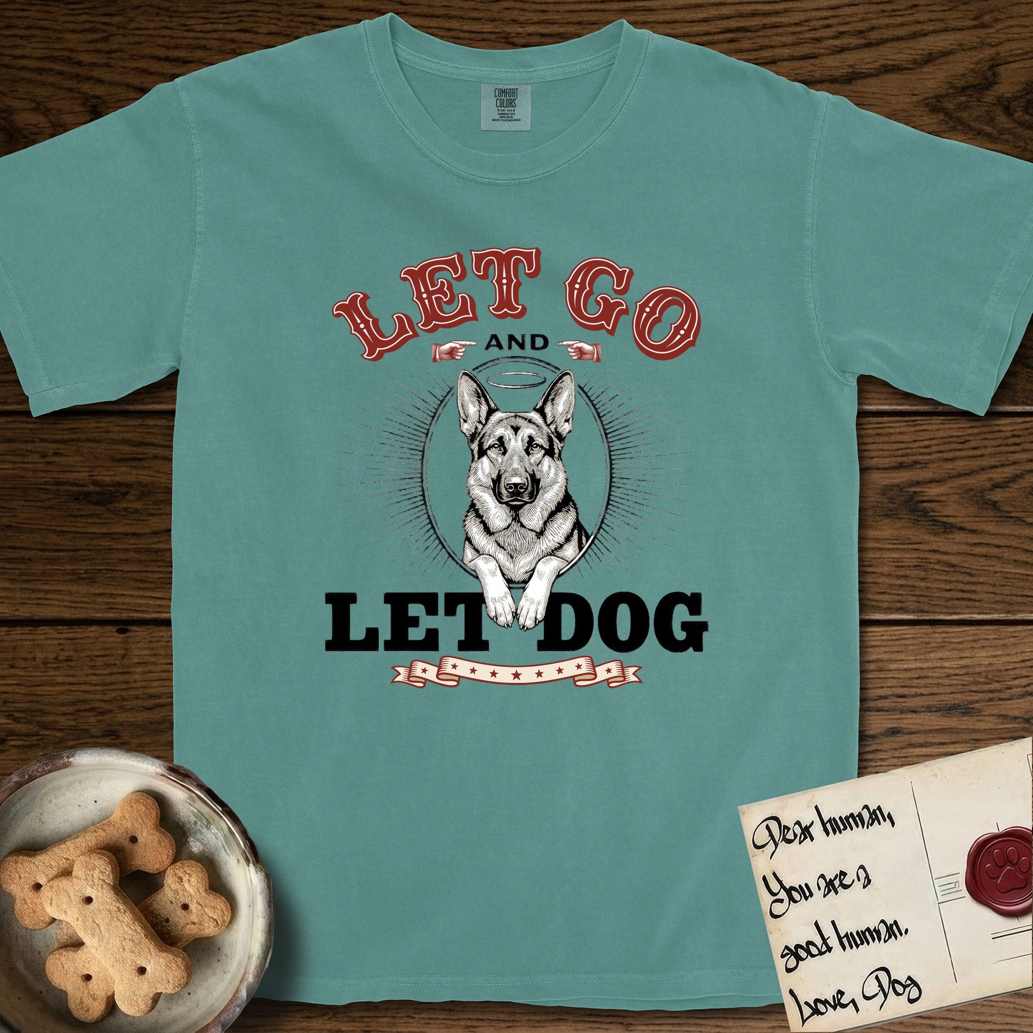 Let Go and Let Dog German Shepherd T-Shirt flat lay in Blue Spruce, featuring a vintage letterpress engraving of a haloed German Shepherd framed by a sunburst oval.