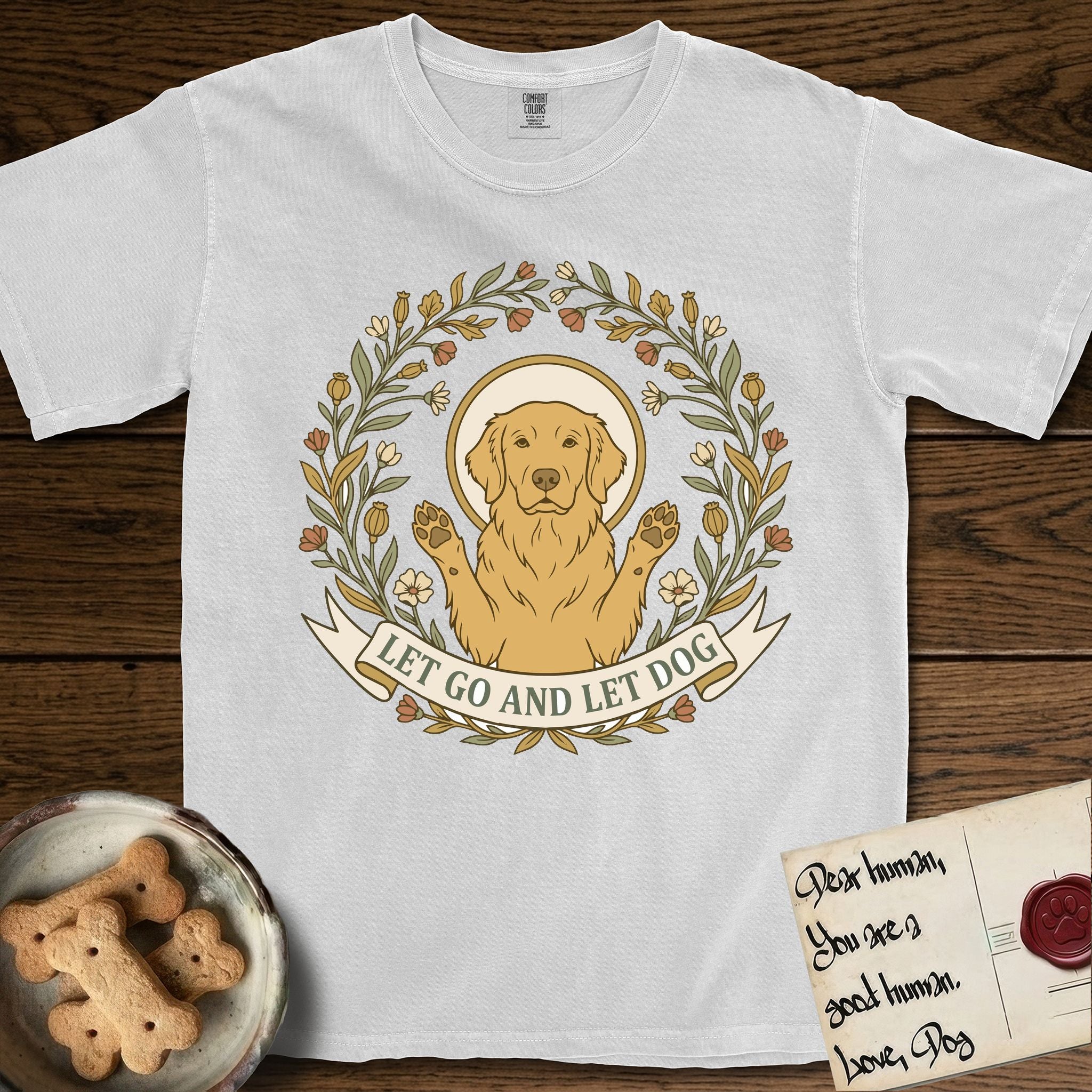 Let Go and Let Dog Golden Retriever T-Shirt flat lay in White, featuring an Art Nouveau wildflower wreath around a haloed Golden Retriever with front paws raised.