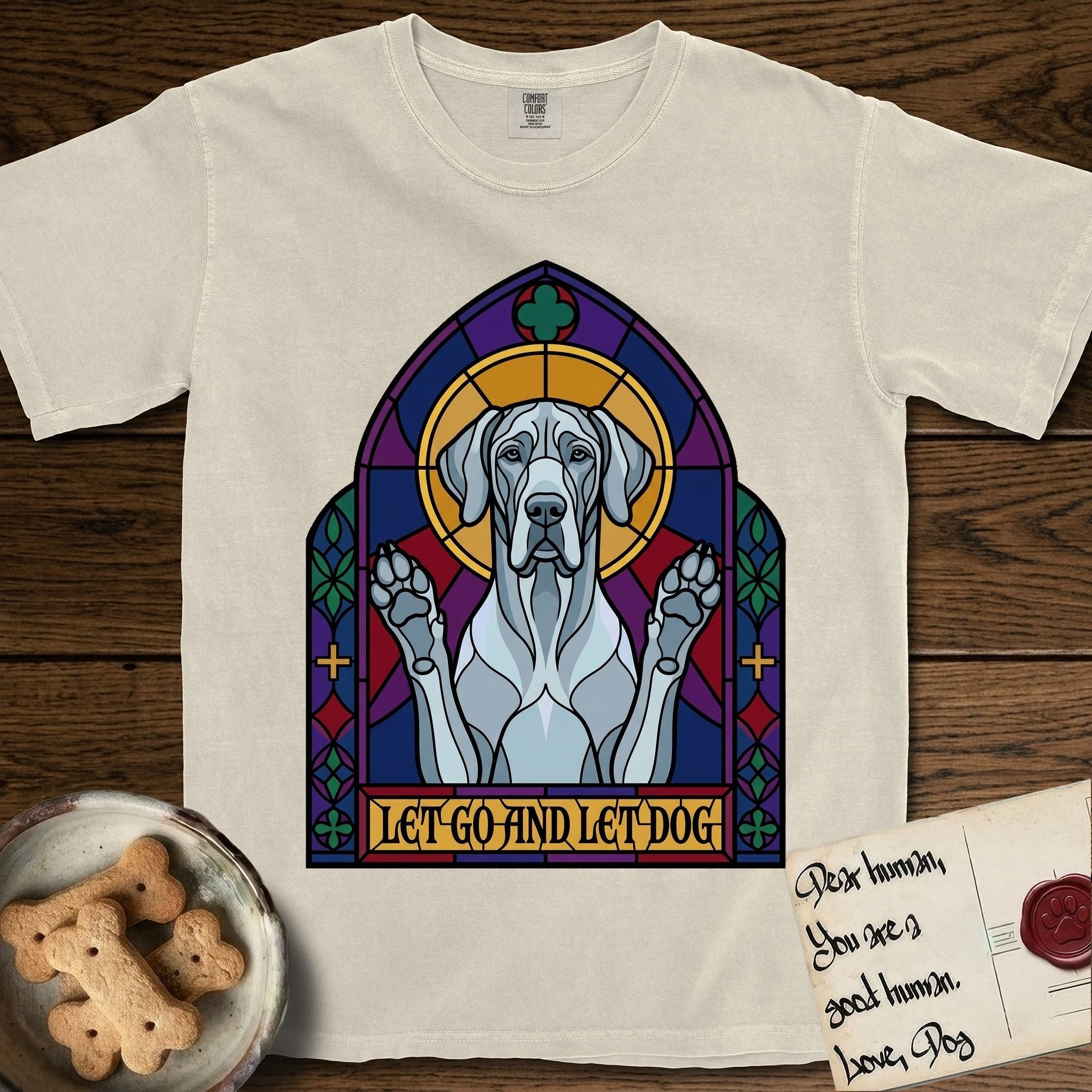 Let Go and Let Dog Great Dane T-Shirt flat lay in Ivory, featuring a stained-glass cathedral window of a haloed Great Dane with paws raised.