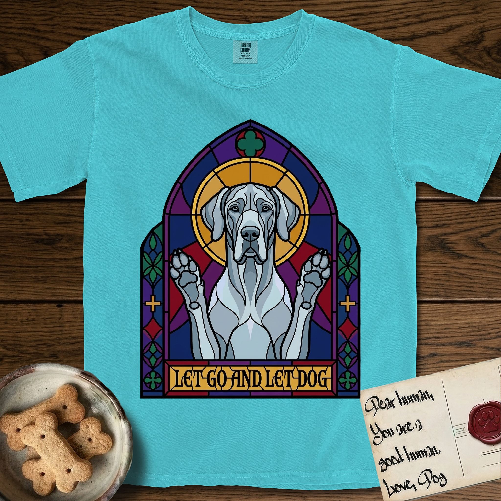 Let Go and Let Dog Great Dane T-Shirt flat lay in Lagoon Blue, featuring a stained-glass cathedral window of a haloed Great Dane with paws raised.