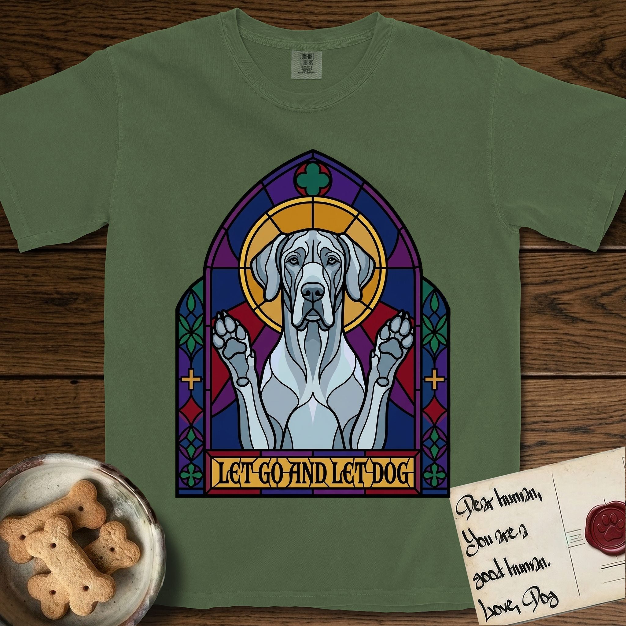 Let Go and Let Dog Great Dane T-Shirt flat lay in Moss, featuring a stained-glass cathedral window of a haloed Great Dane with paws raised.