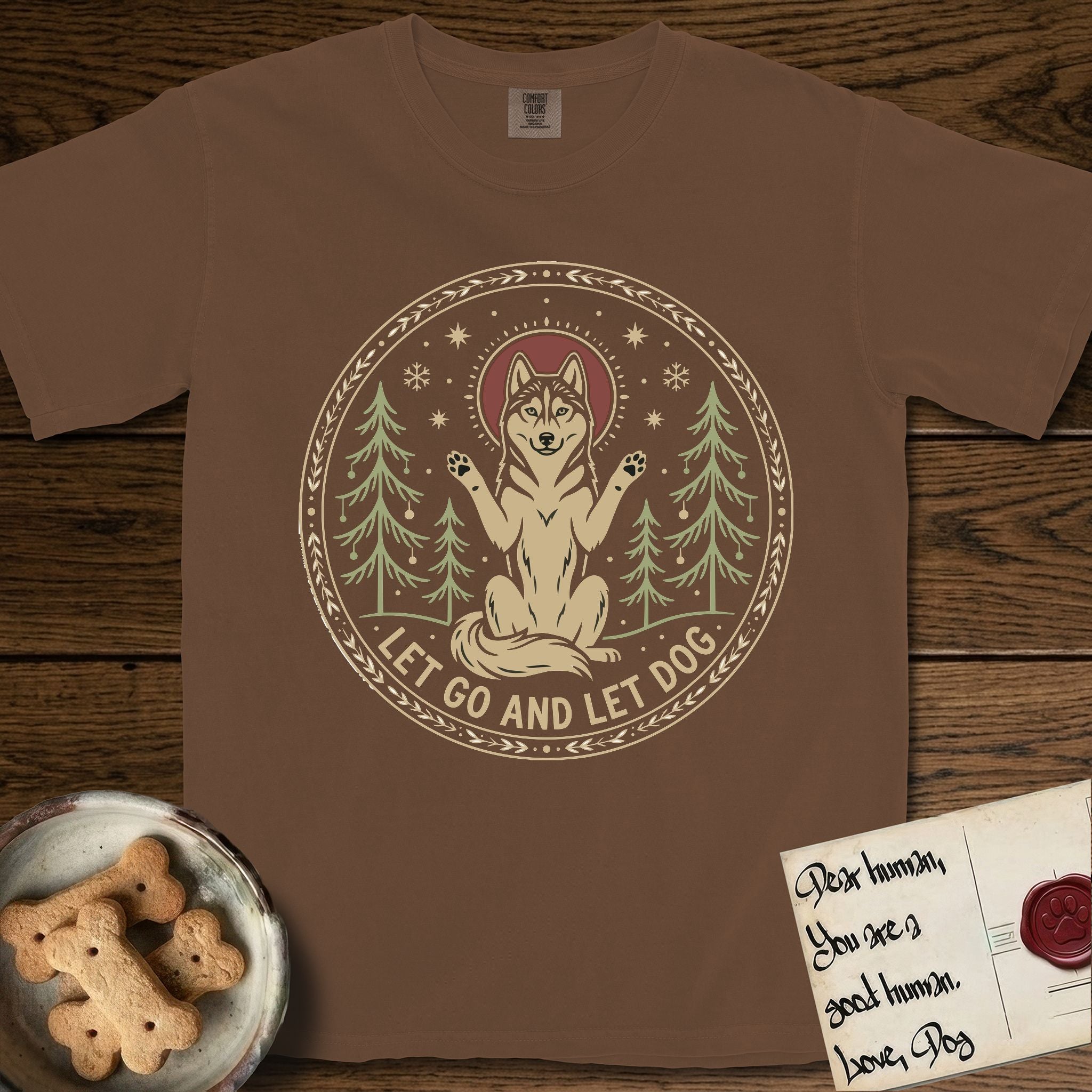 Let Go and Let Dog Husky T-Shirt flat lay in Espresso, featuring a winter woodland seal of a haloed Husky sitting with paws raised among pine trees.