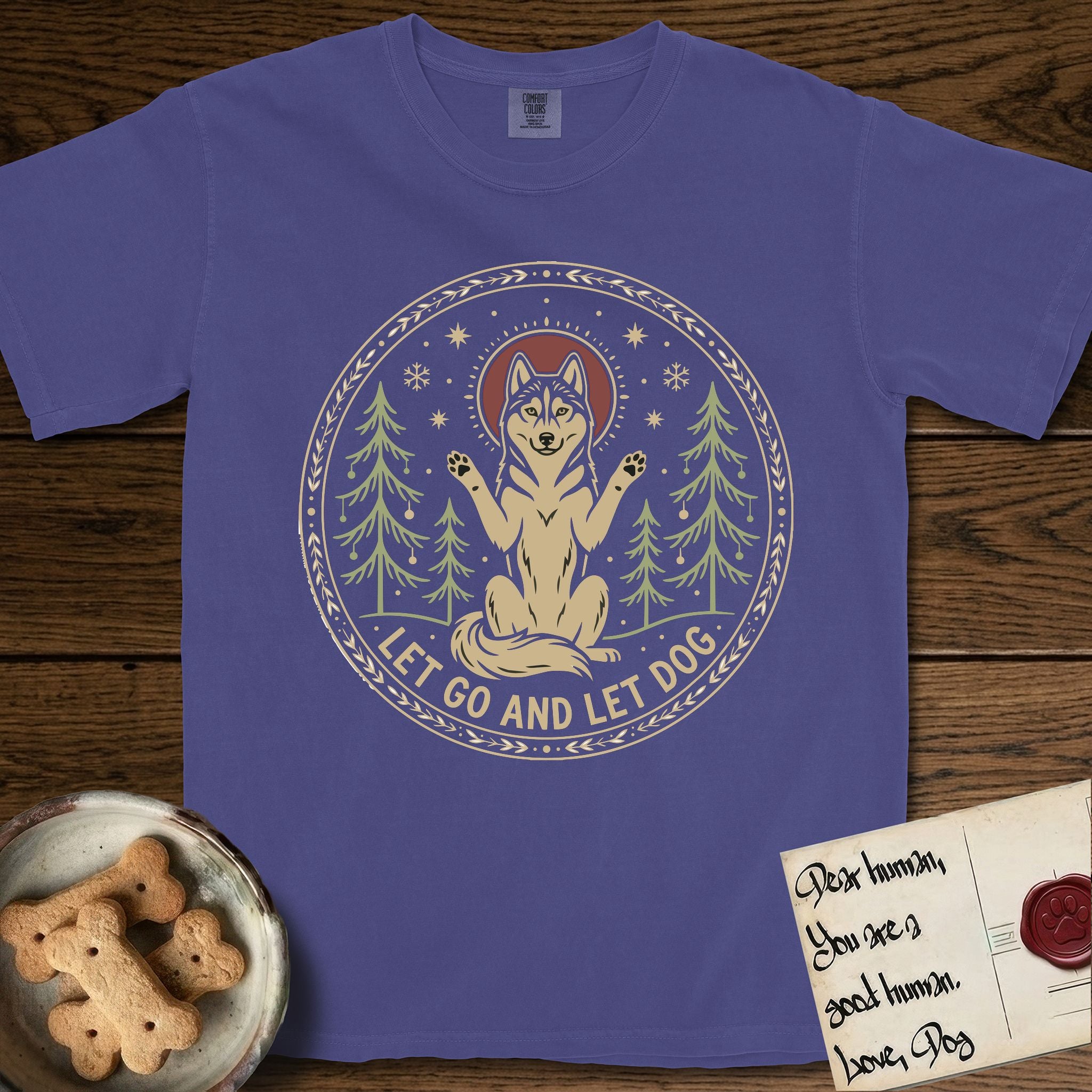 Let Go and Let Dog Husky T-Shirt flat lay in Grape, featuring a winter woodland seal of a haloed Husky sitting with paws raised among pine trees.