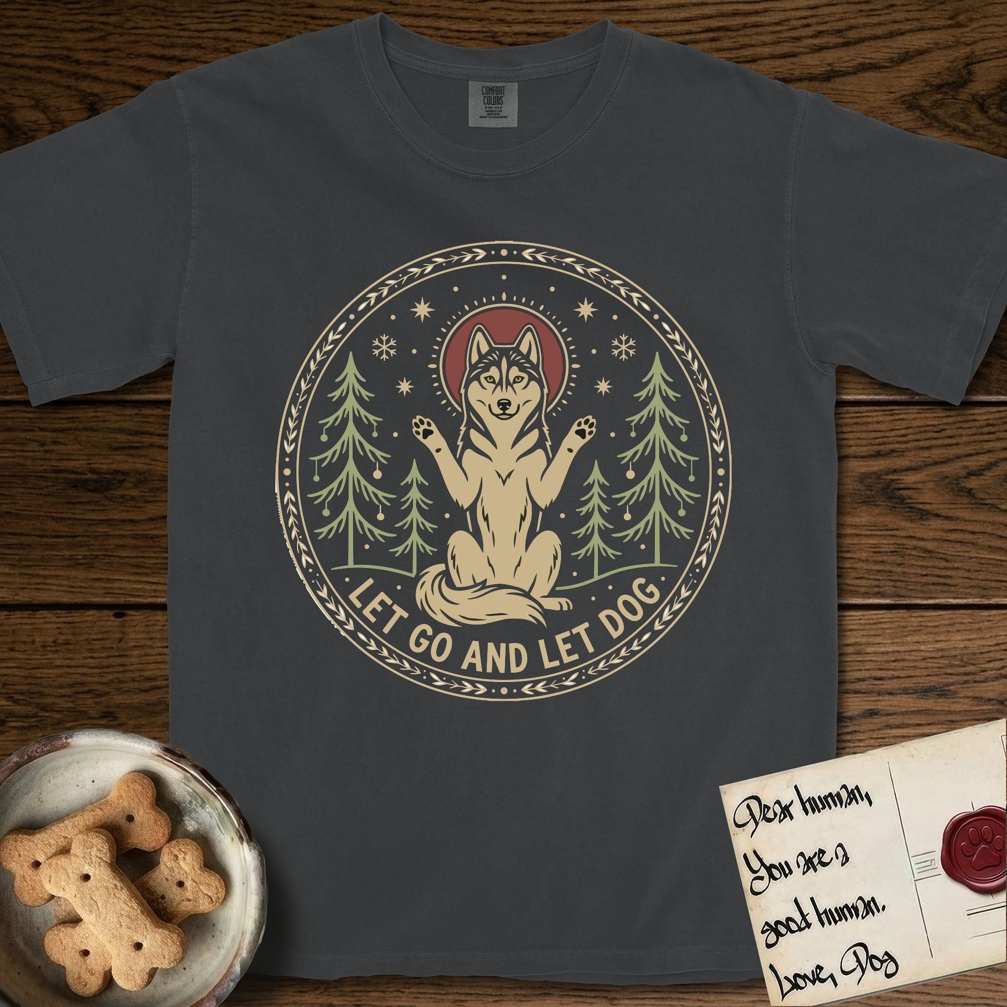 Let Go and Let Dog Husky T-Shirt flat lay in Graphite, featuring a winter woodland seal of a haloed Husky sitting with paws raised among pine trees.