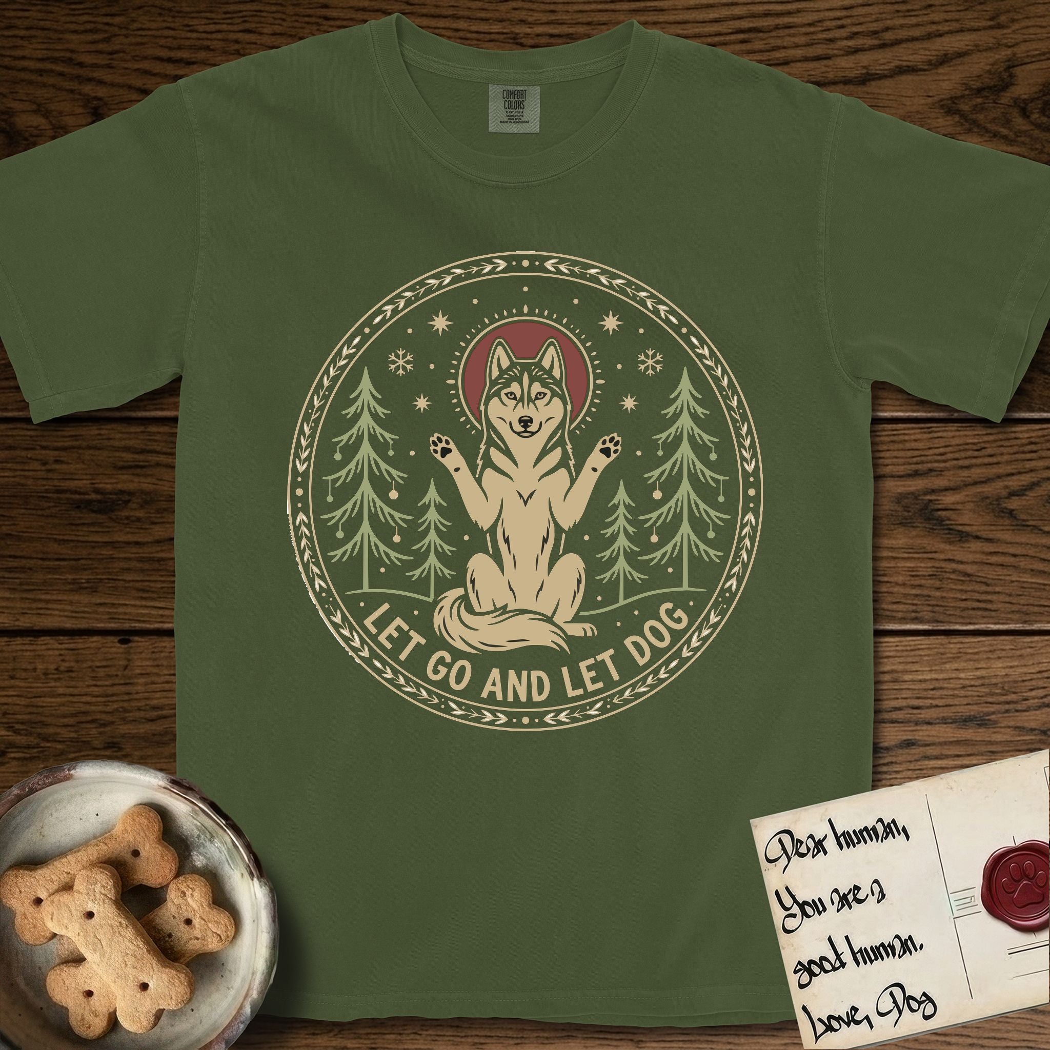 Let Go and Let Dog Husky T-Shirt flat lay in Hemp, featuring a winter woodland seal of a haloed Husky sitting with paws raised among pine trees.