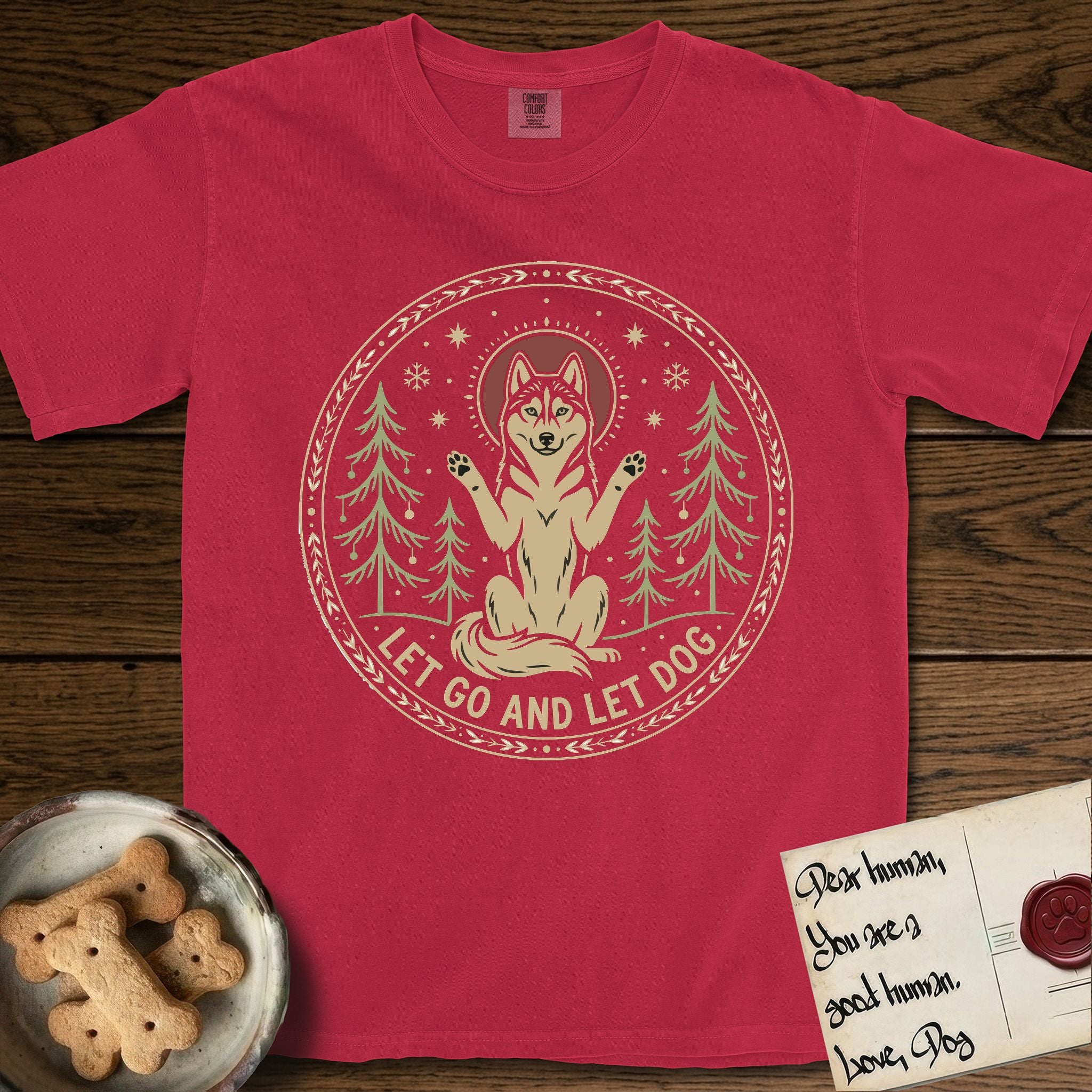 Let Go and Let Dog Husky T-Shirt flat lay in Red, featuring a winter woodland seal of a haloed Husky sitting with paws raised among pine trees.