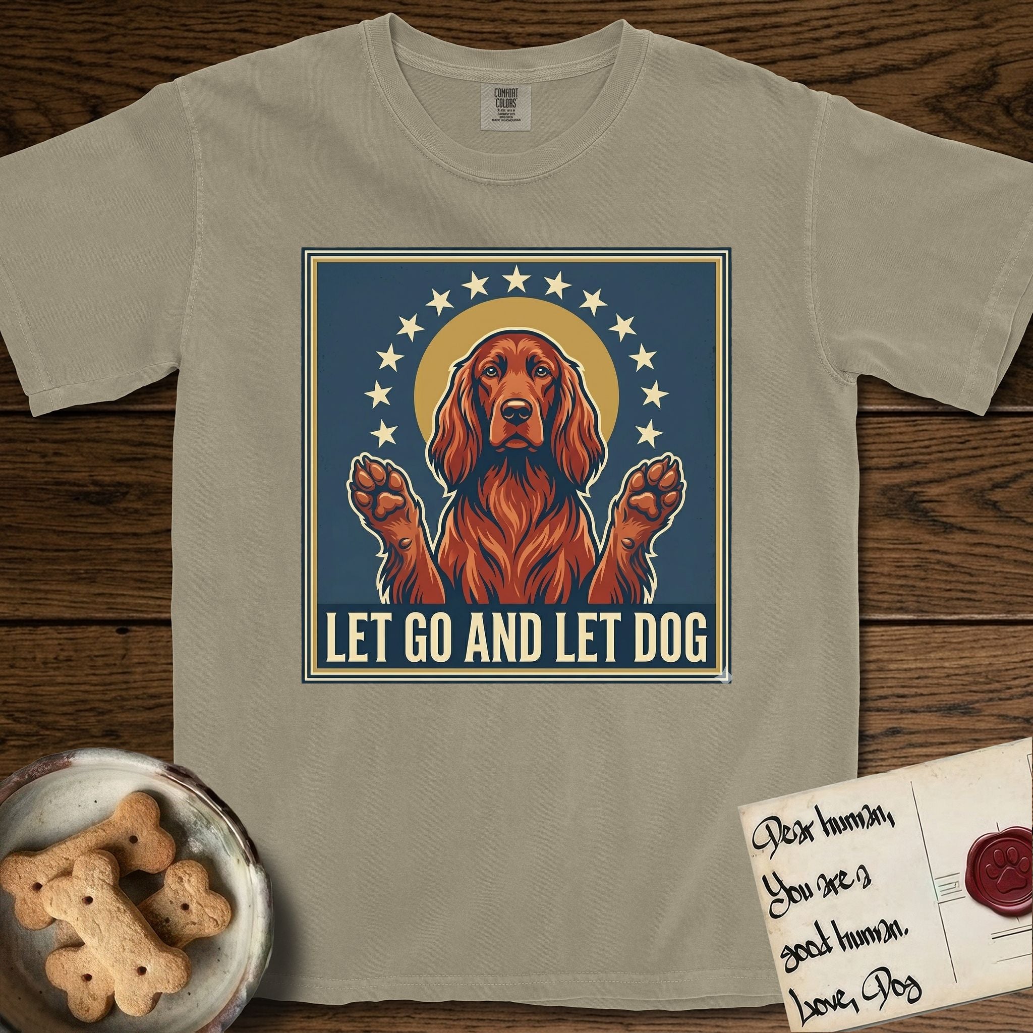 Let Go and Let Dog Irish Setter T-Shirt flat lay in Khaki, featuring a vintage devotional poster of a haloed Irish Setter with paws raised and a ring of stars.