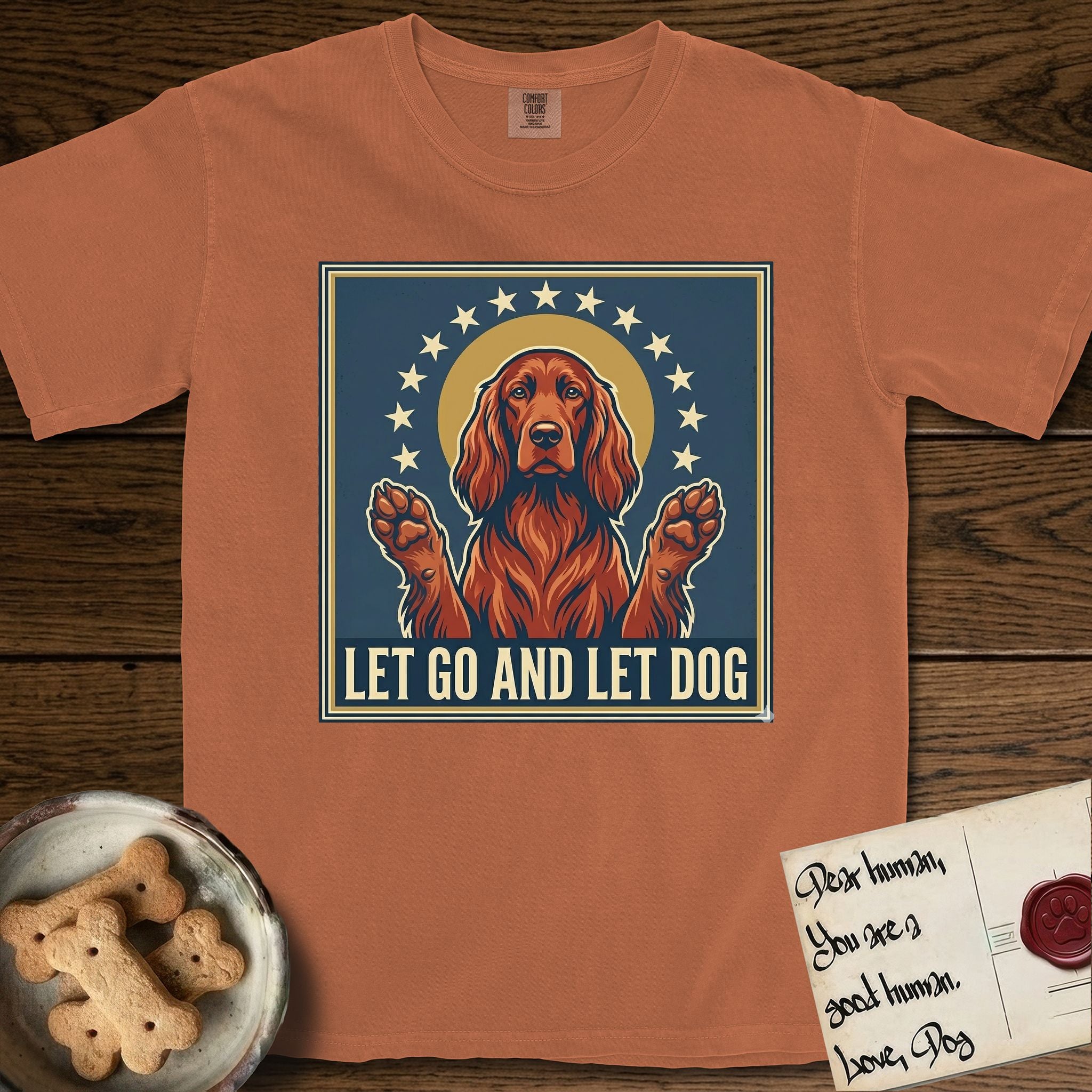 Let Go and Let Dog Irish Setter T-Shirt flat lay in Yam, featuring a vintage devotional poster of a haloed Irish Setter with paws raised and a ring of stars.