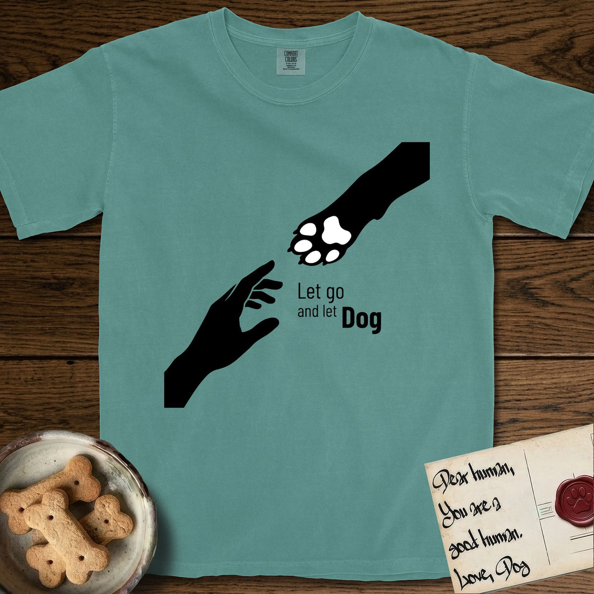 Let Go and Let Dog Paw T-Shirt flat lay in Blue Spruce, featuring a minimalist silhouette of a human hand and a Dog paw reaching toward each other, almost touching.