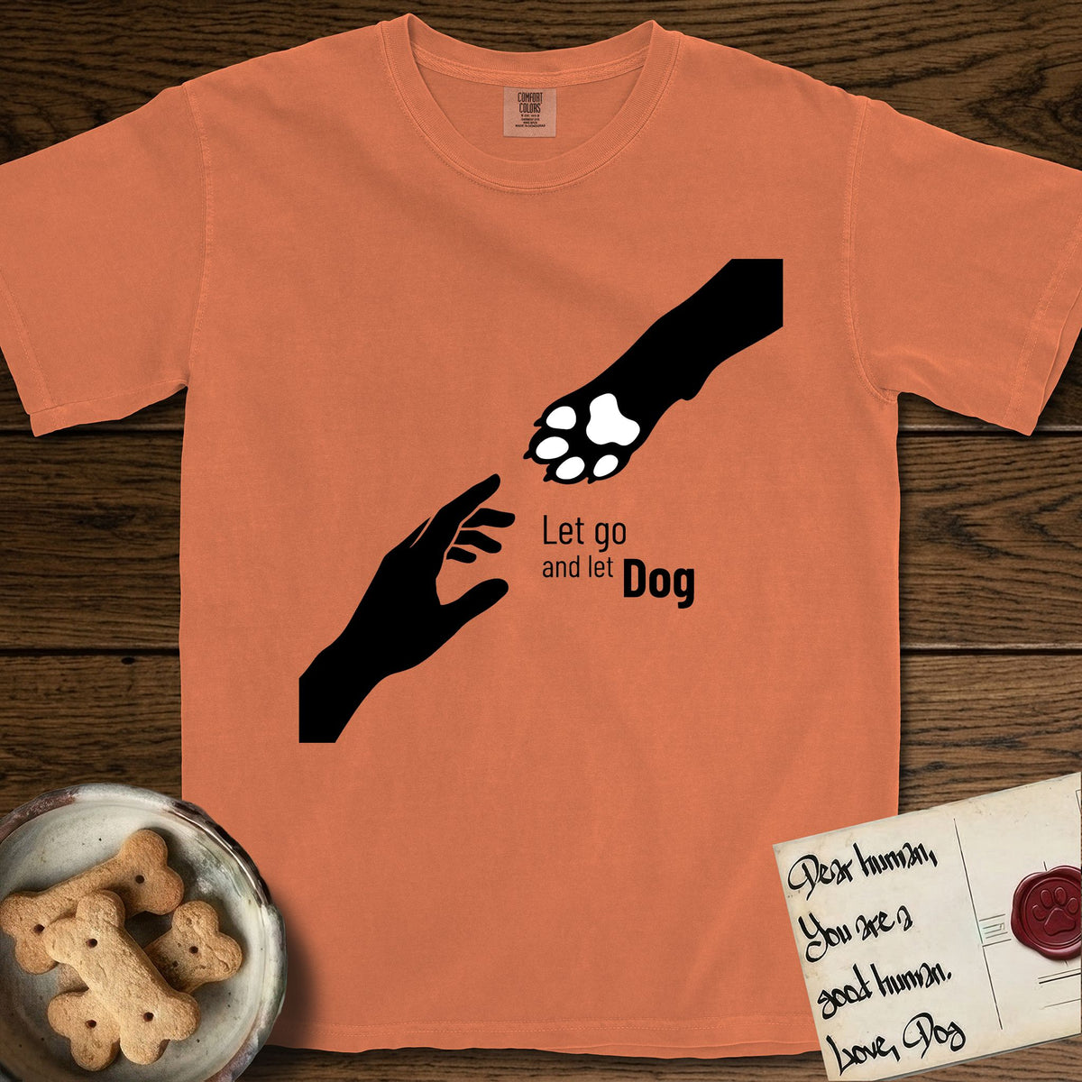 Let Go and Let Dog Paw T-Shirt flat lay in Melon, featuring a minimalist silhouette of a human hand and a Dog paw reaching toward each other, almost touching.