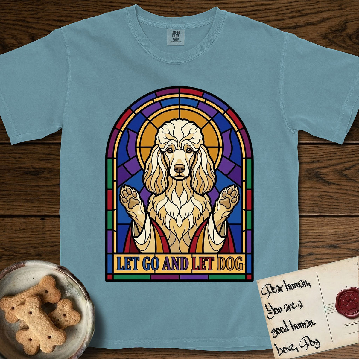 Let Go and Let Dog Poodle T-Shirt flat lay in Ice Blue, featuring a stained-glass illustration of a haloed Poodle with paws raised.