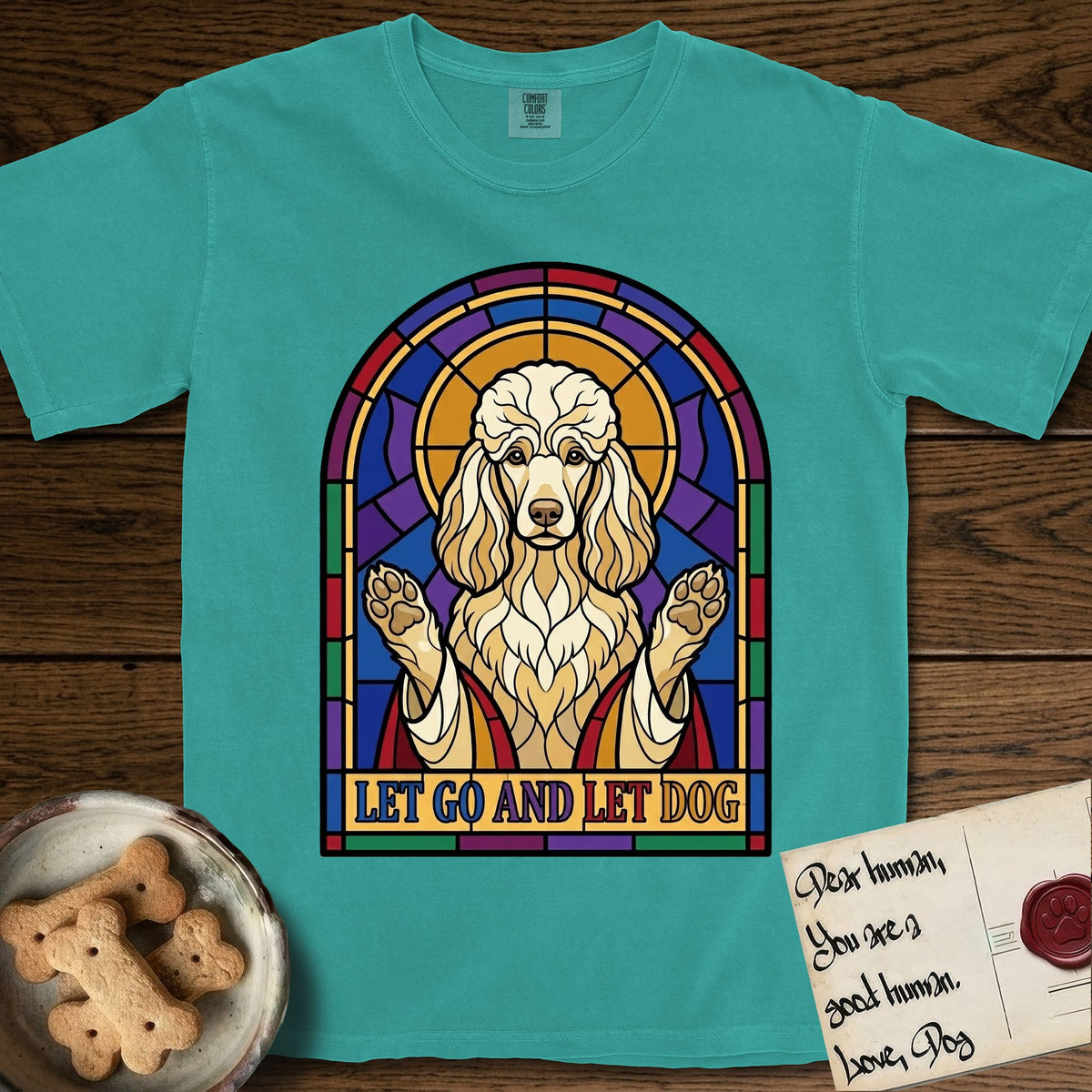 Let Go and Let Dog Poodle T-Shirt flat lay in Seafoam, featuring a stained-glass illustration of a haloed Poodle with paws raised.
