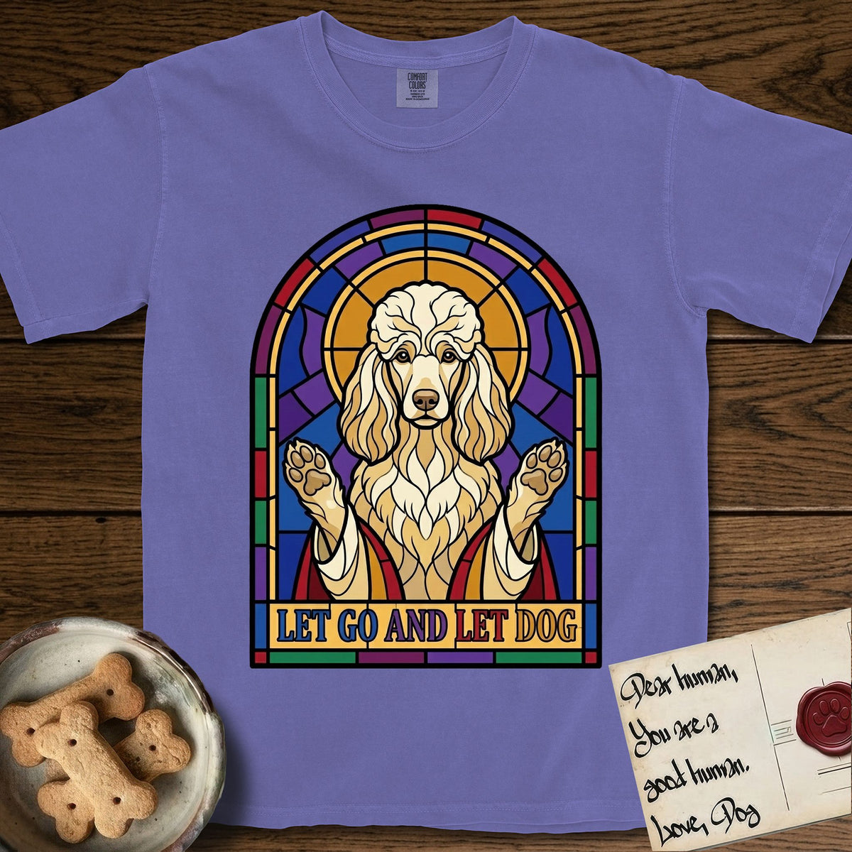 Let Go and Let Dog Poodle T-Shirt flat lay in Violet, featuring a stained-glass illustration of a haloed Poodle with paws raised.