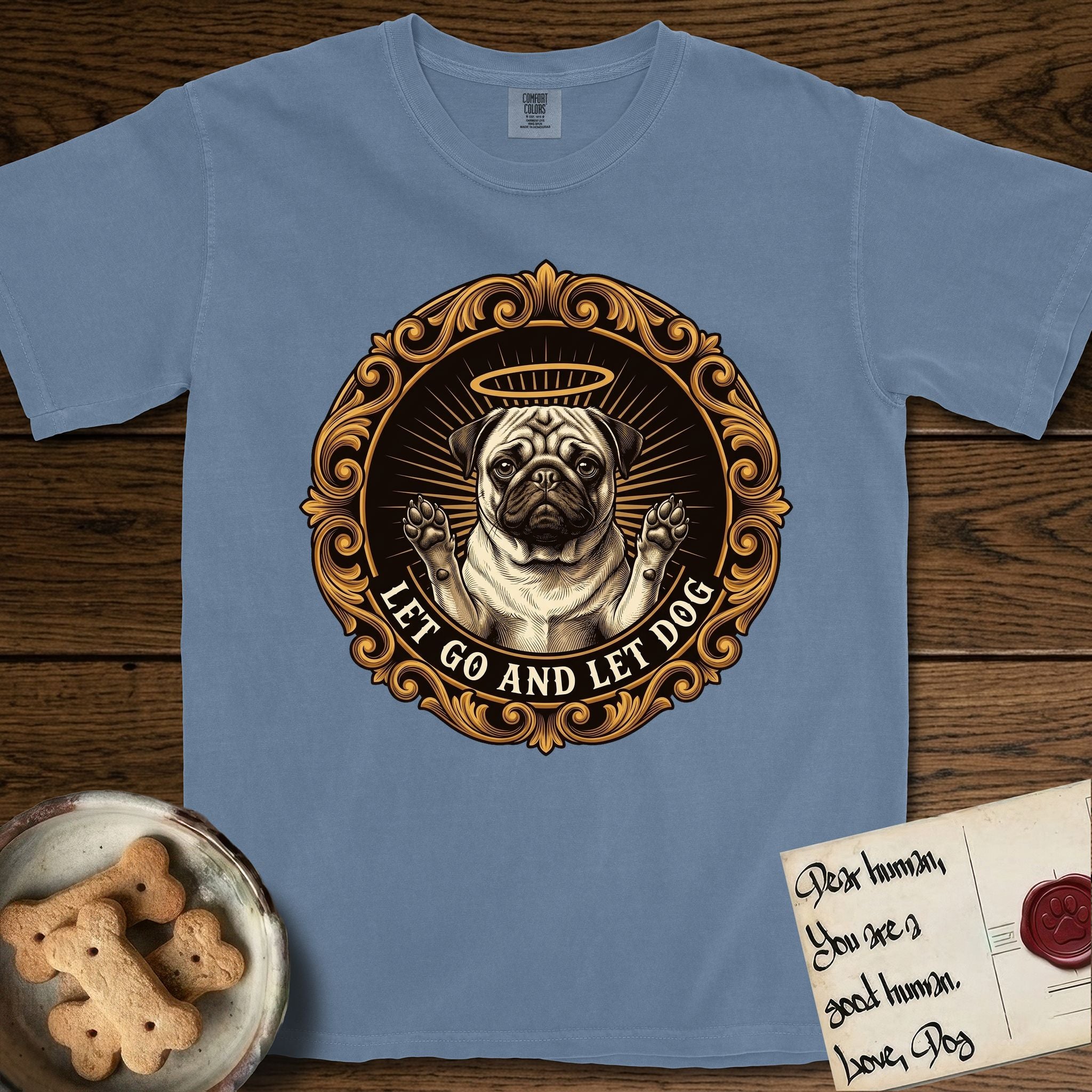 Let Go and Let Dog Pug T-Shirt flat lay in Blue Jean, featuring a baroque medallion engraving of a haloed Pug with paws raised, framed in gold scrollwork.