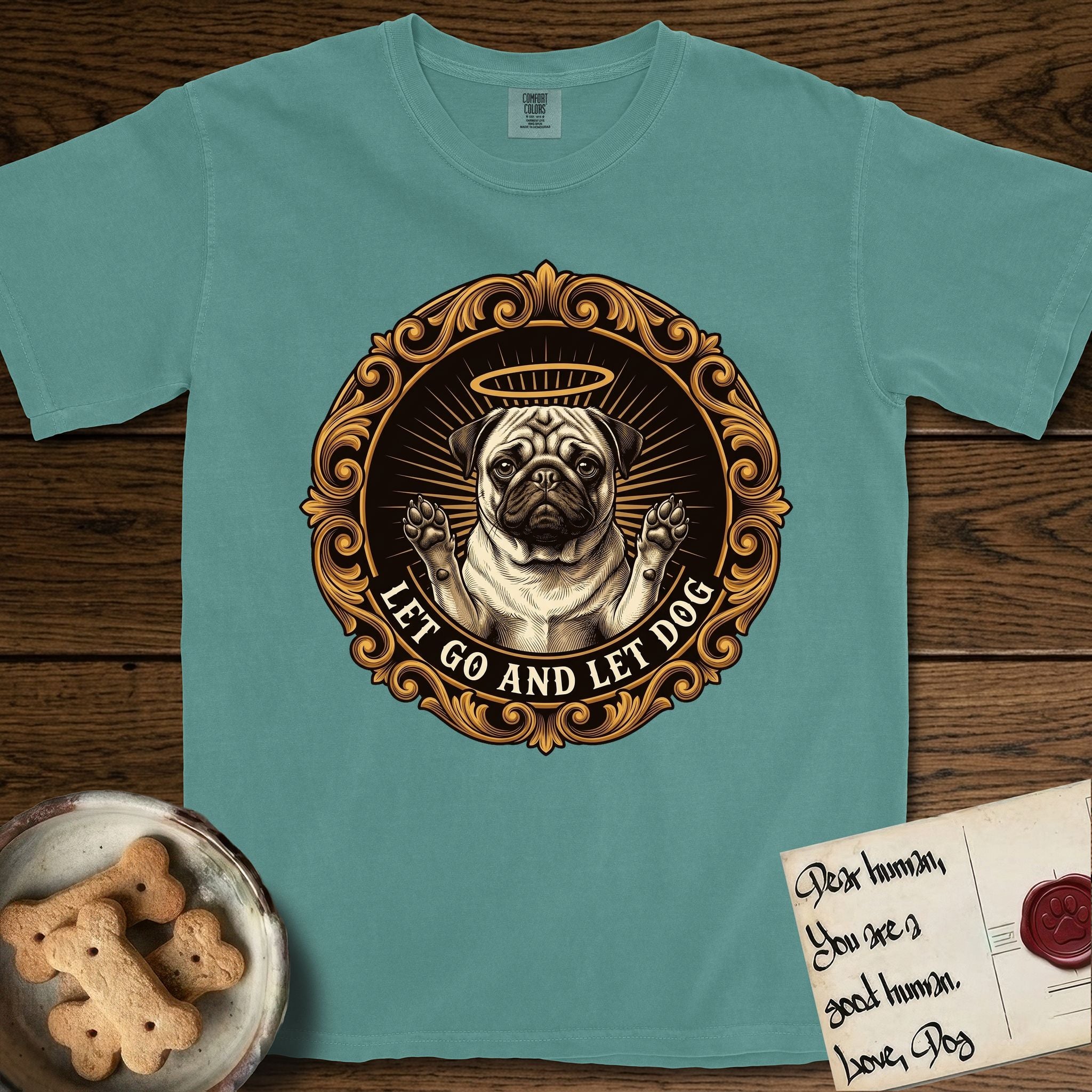 Let Go and Let Dog Pug T-Shirt flat lay in Blue Spruce, featuring a baroque medallion engraving of a haloed Pug with paws raised, framed in gold scrollwork.