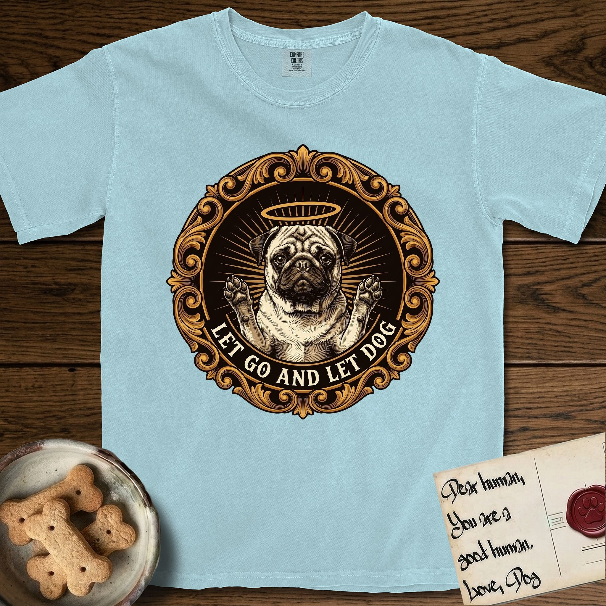 Let Go and Let Dog Pug T-Shirt flat lay in Chambray, featuring a baroque medallion engraving of a haloed Pug with paws raised, framed in gold scrollwork.